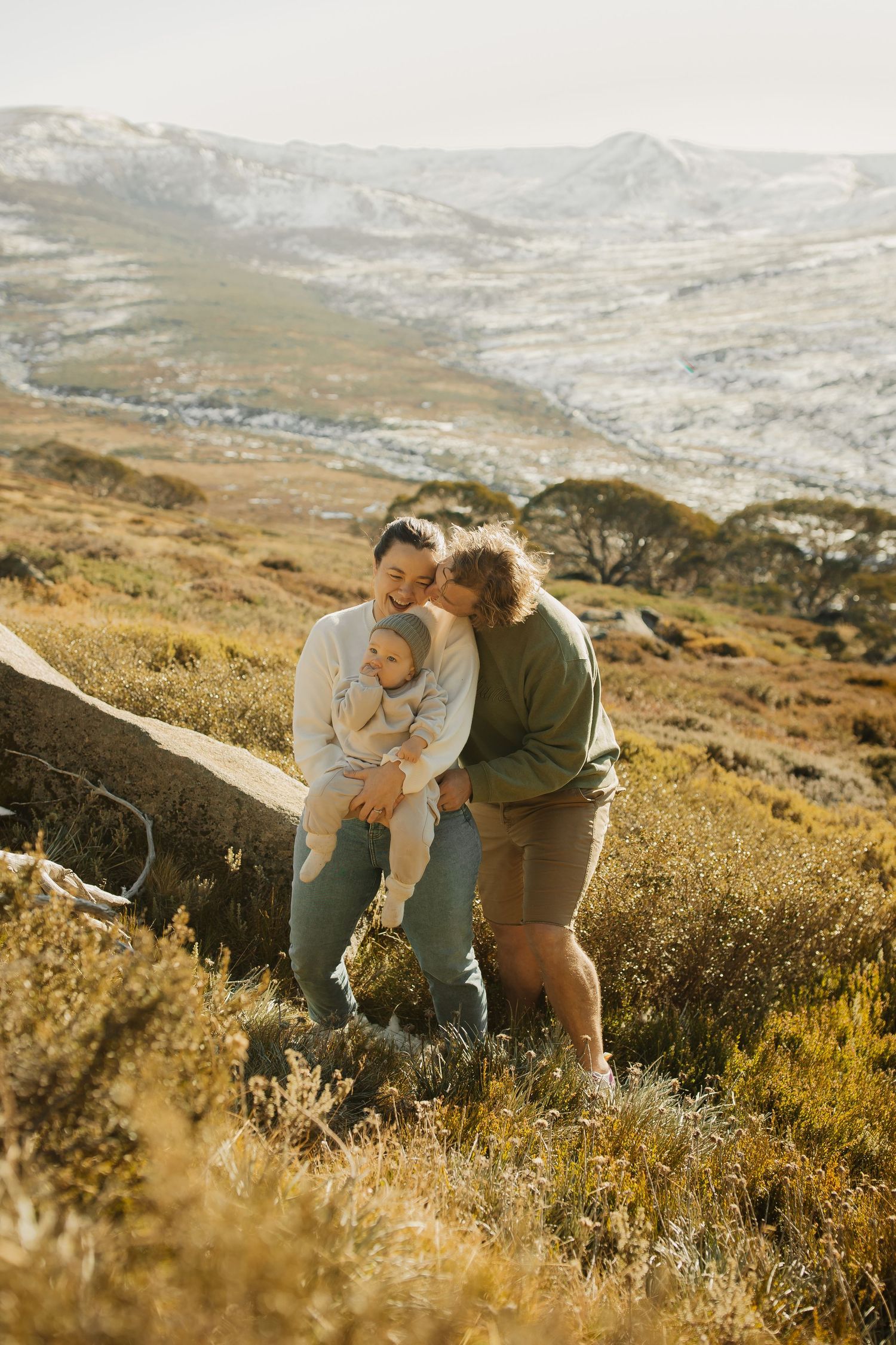 Two people share an intimate moment together while sitting on rocks in a sunny mountainous landscape at golden hour.