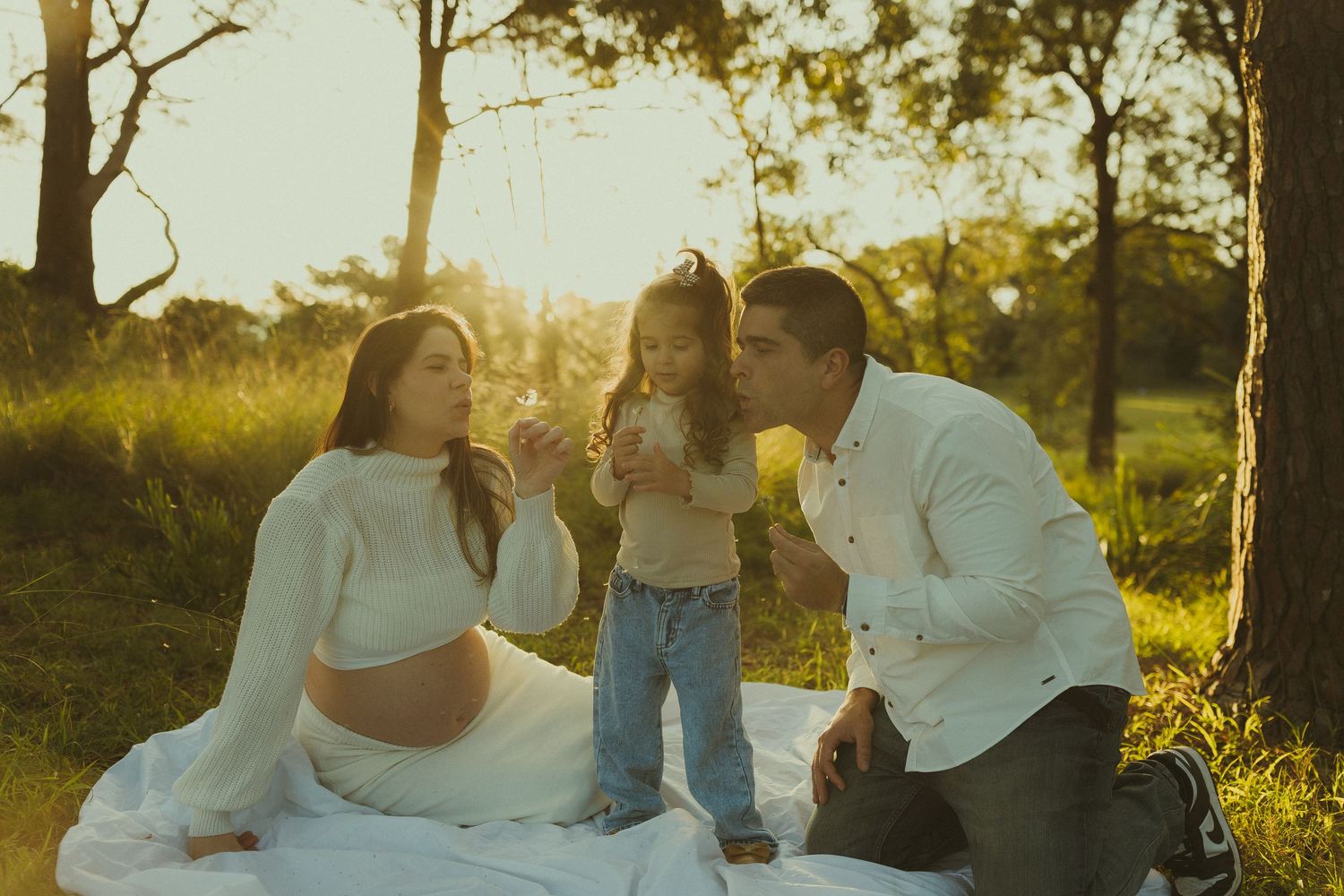 Family enjoying a picnic on white blanket during golden hour in a grassy field.