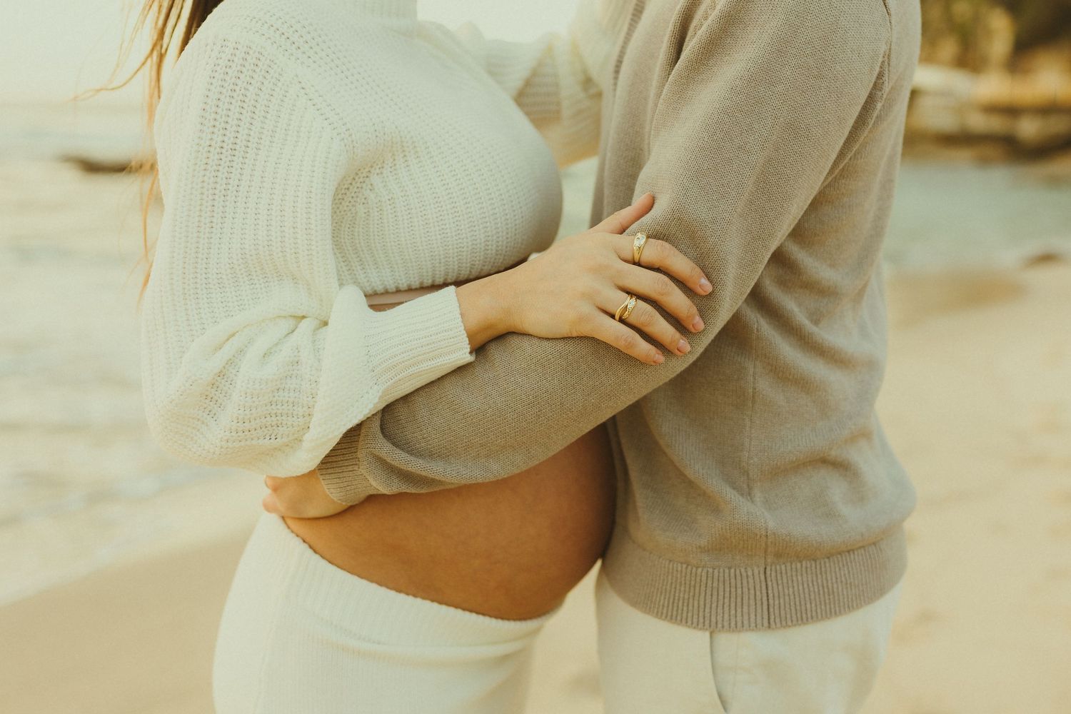 A close-up shot of two people embracing while wearing cozy sweaters in soft muted tones.