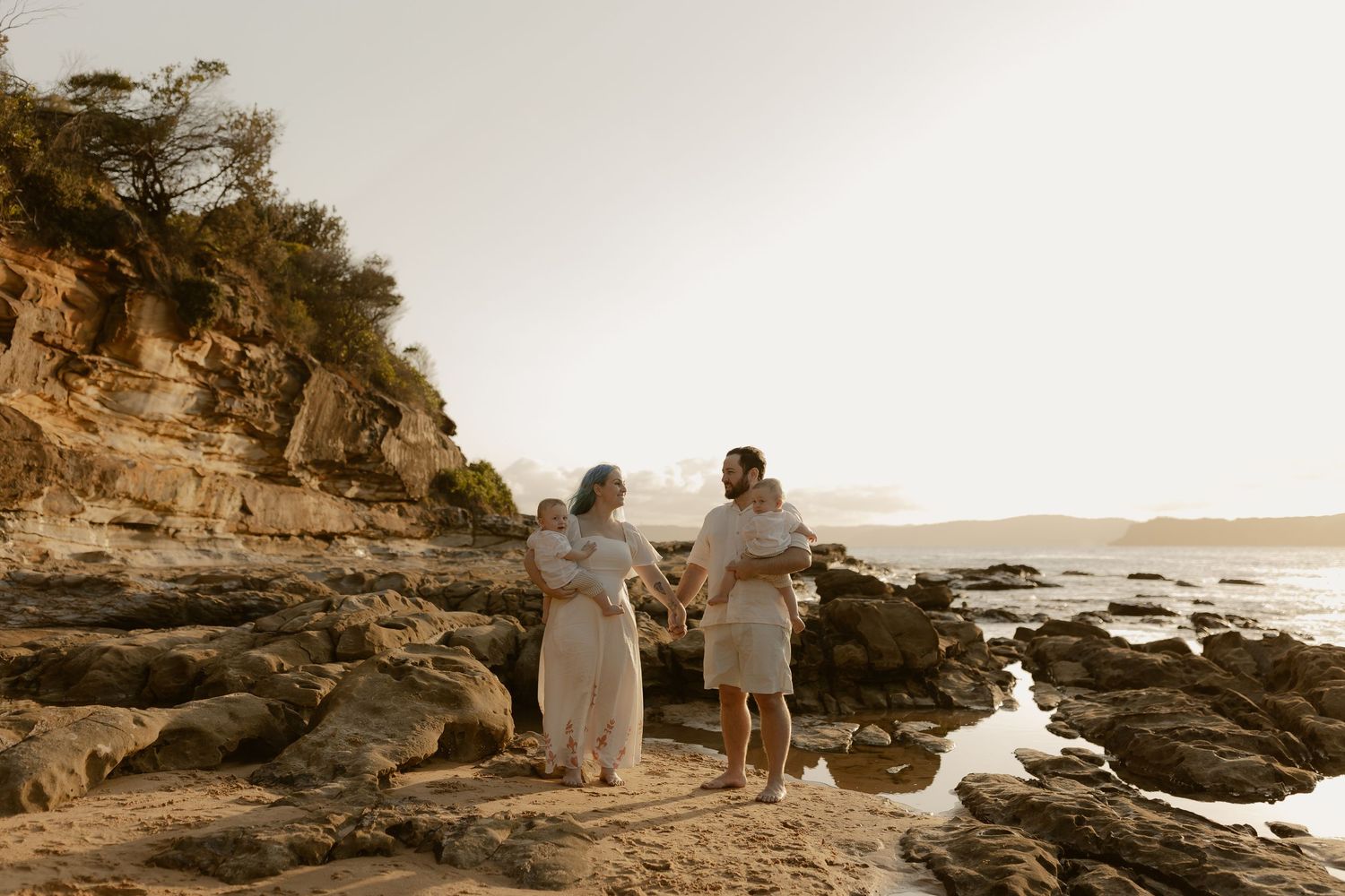 A couple walks along a rocky coastal shoreline at sunset creating a romantic silhouette against the golden sky.