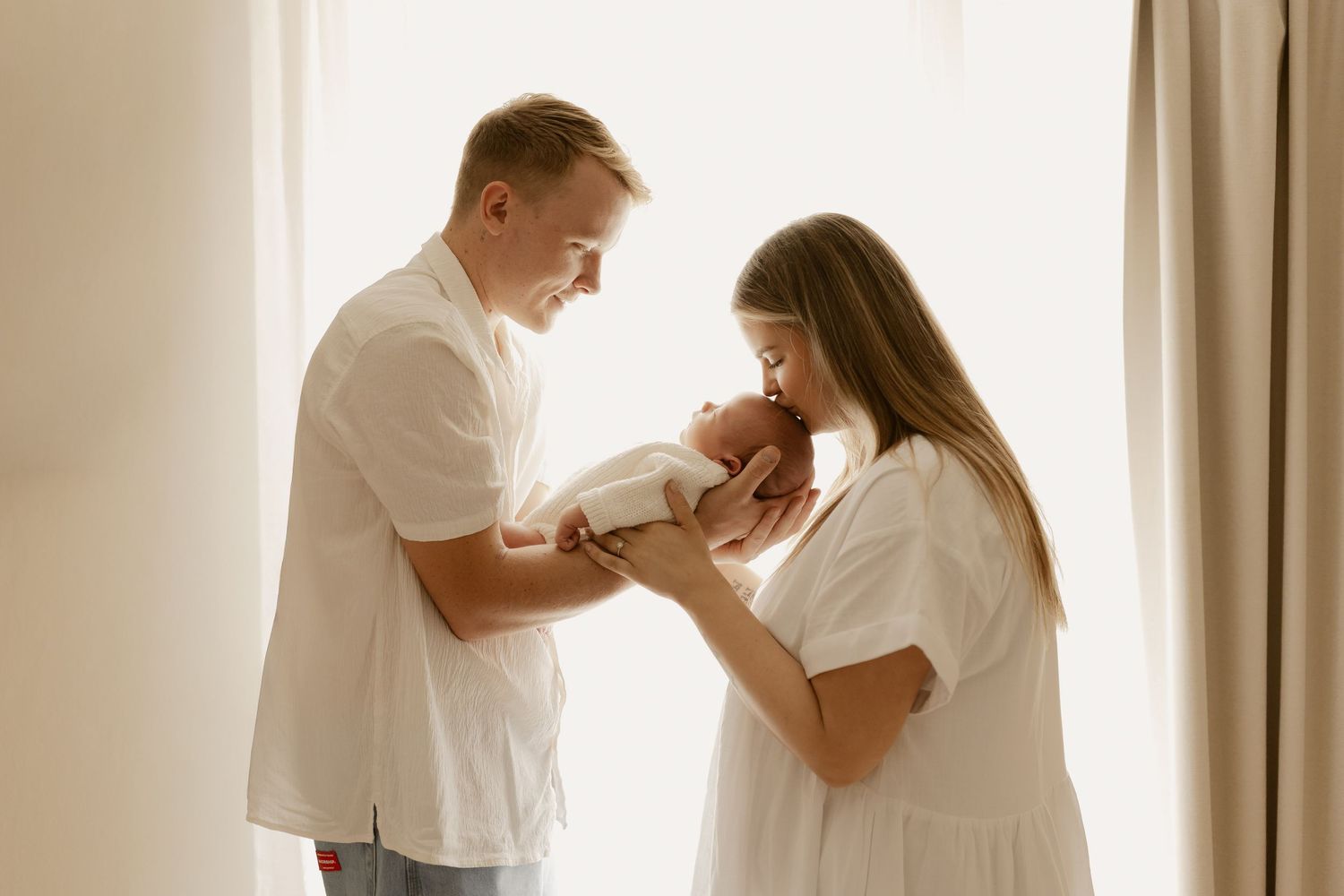 A tender moment between parents as they gaze lovingly at their newborn baby in a softly lit room.