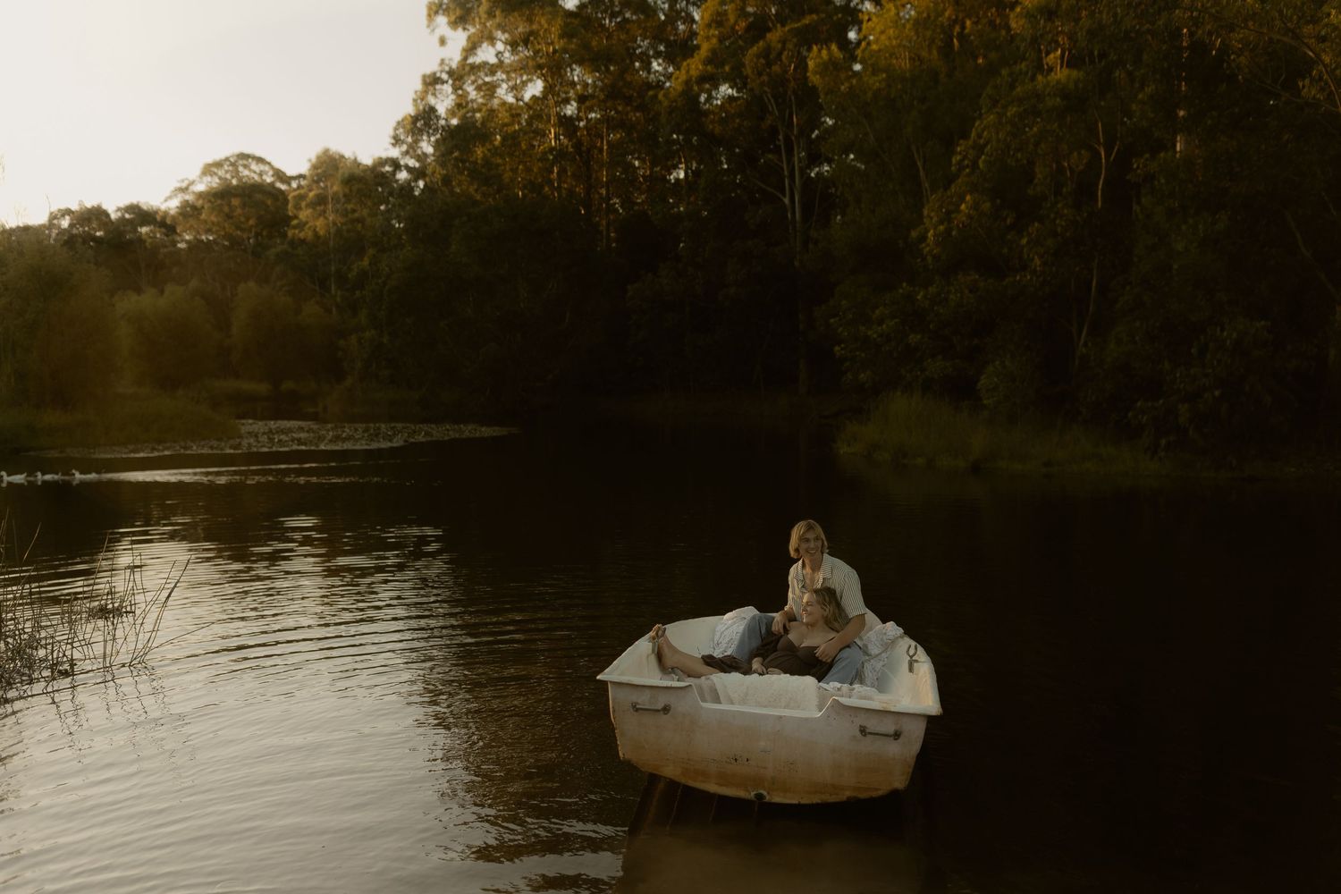 Small white boat floating on calm waters during golden hour with trees in background.