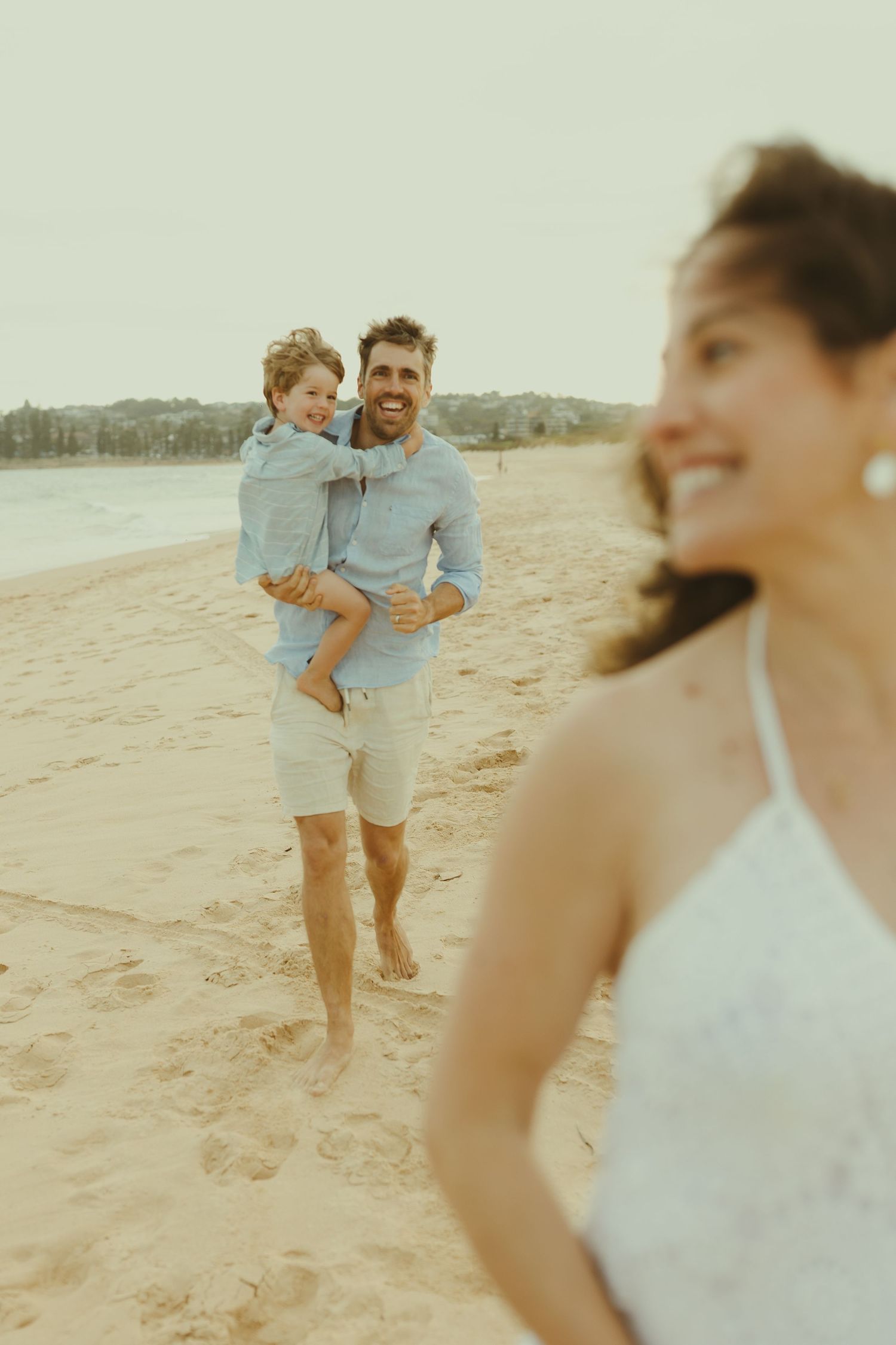 Playful family moments unfold on a sunlit beach during a photo session.