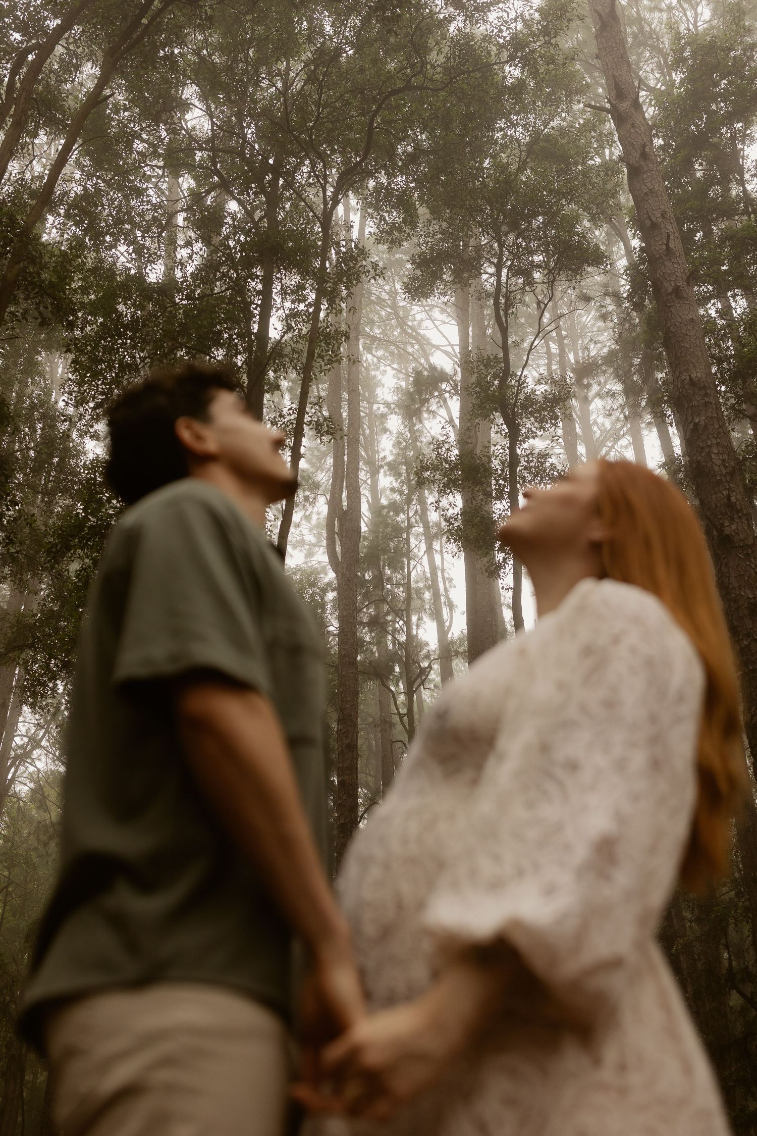An intimate forest maternity session captures a couple dancing together in soft, filtered light.