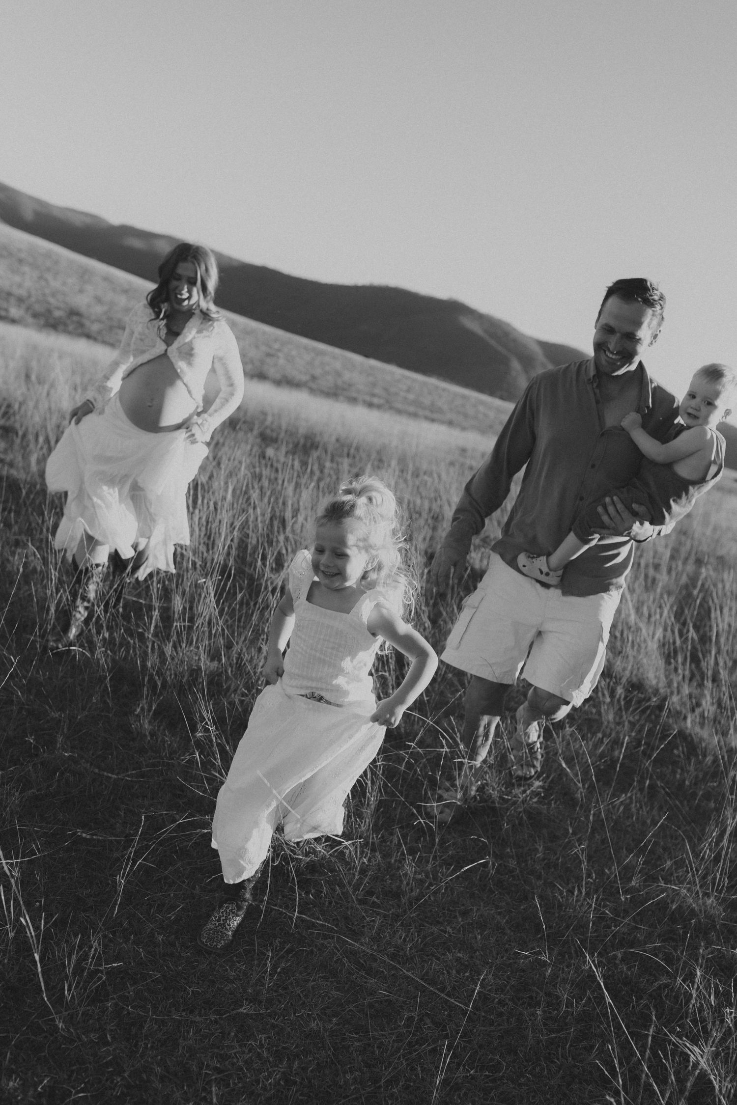 Black and white photo of a family running through a grassy field with mountains in the background.