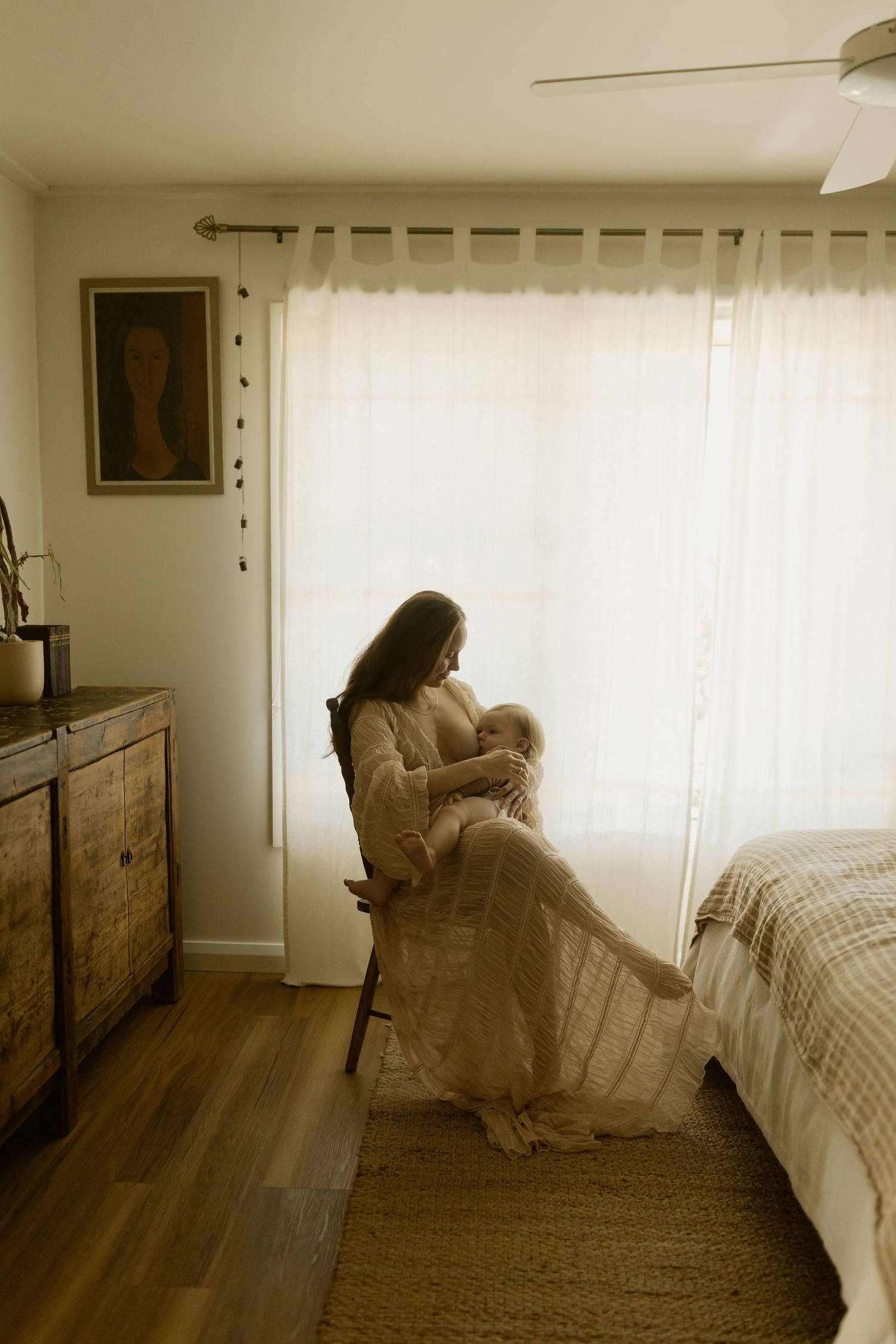 Intimate lifestyle photography session in a sunlit bedroom with soft natural warmth and vintage wood furniture.