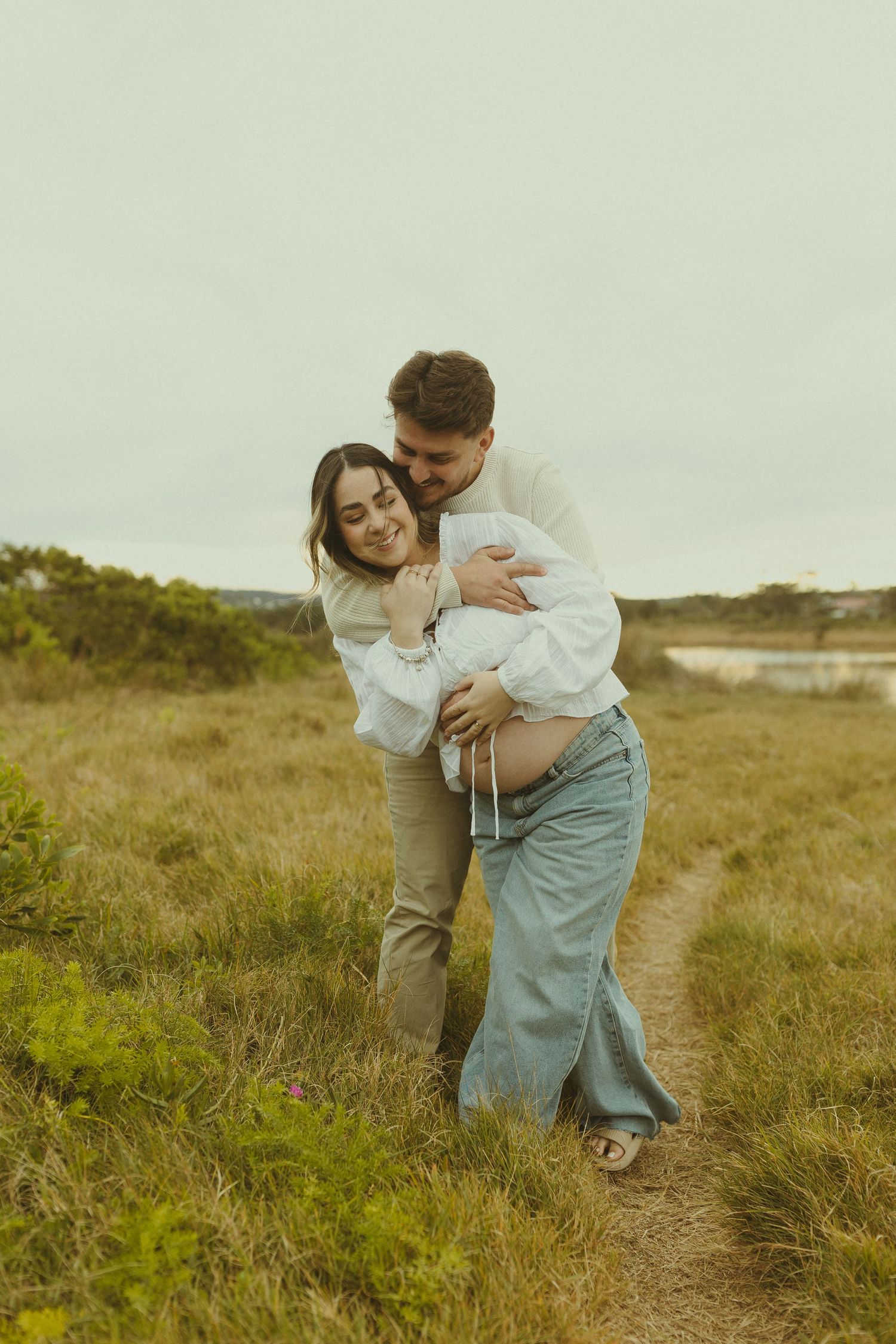 A romantic couple shares a tender moment embracing on a grassy hilltop during golden hour.