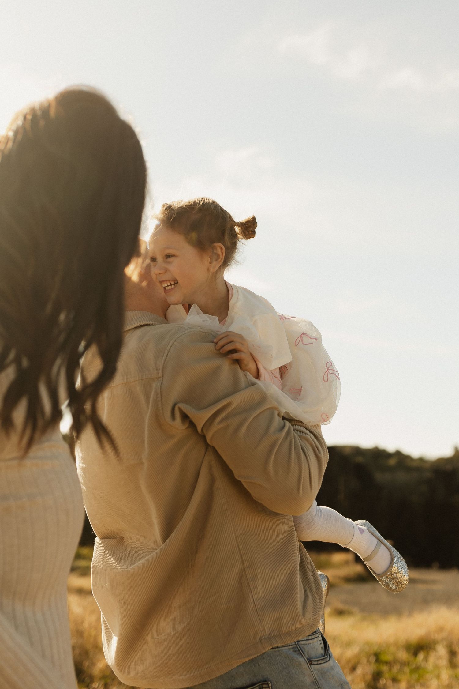 A joyful moment captured in golden light as a pair shares laughter and embraces in an outdoor field setting.