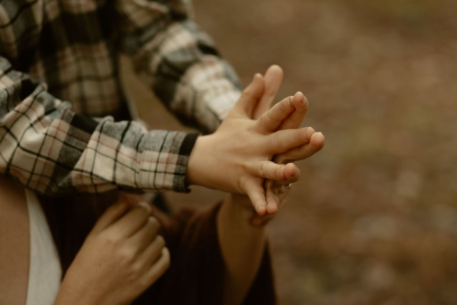 Close-up of hands touching in warm sunlight, wearing plaid clothing.