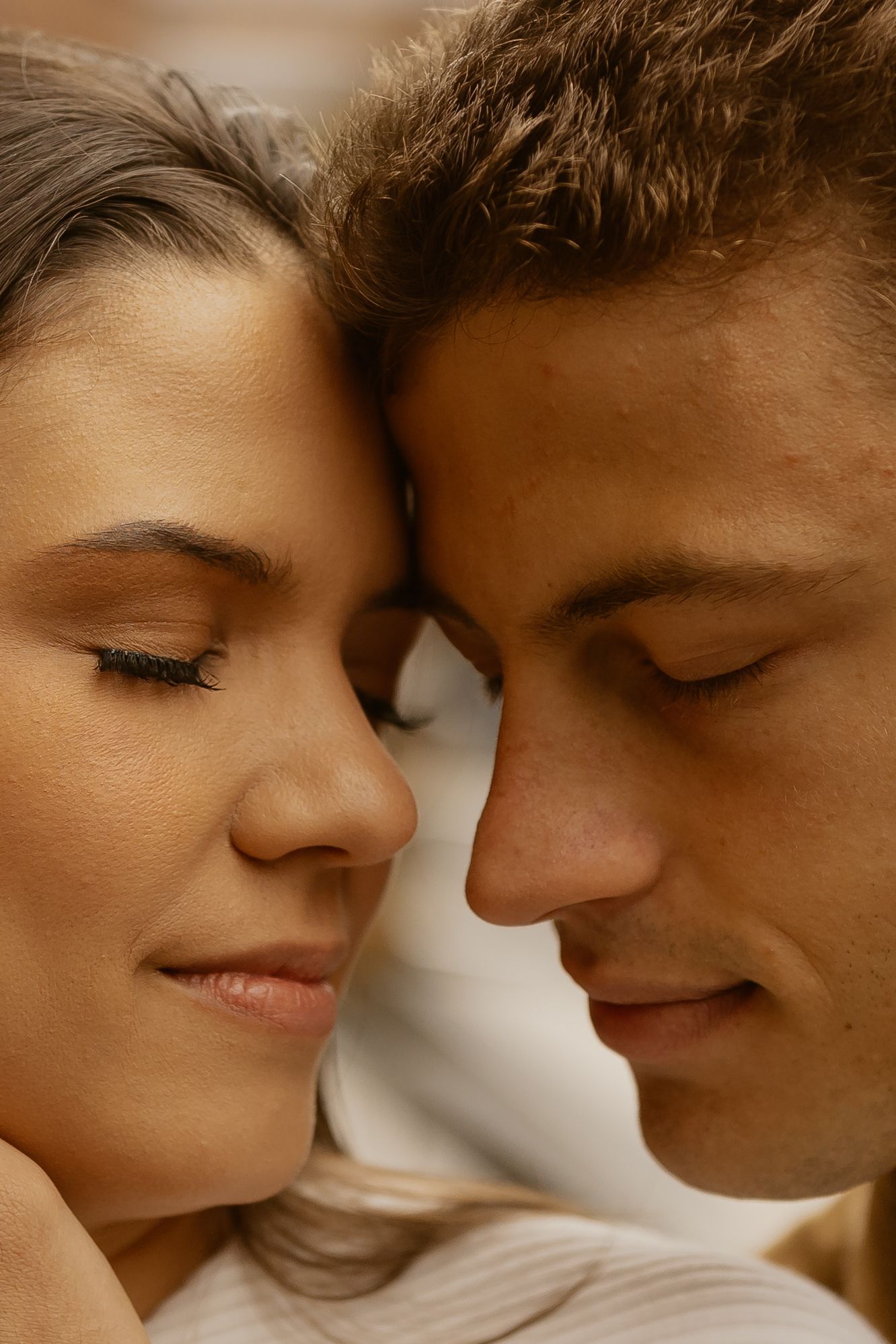 Intimate close-up of couple with foreheads touching in warm lighting.