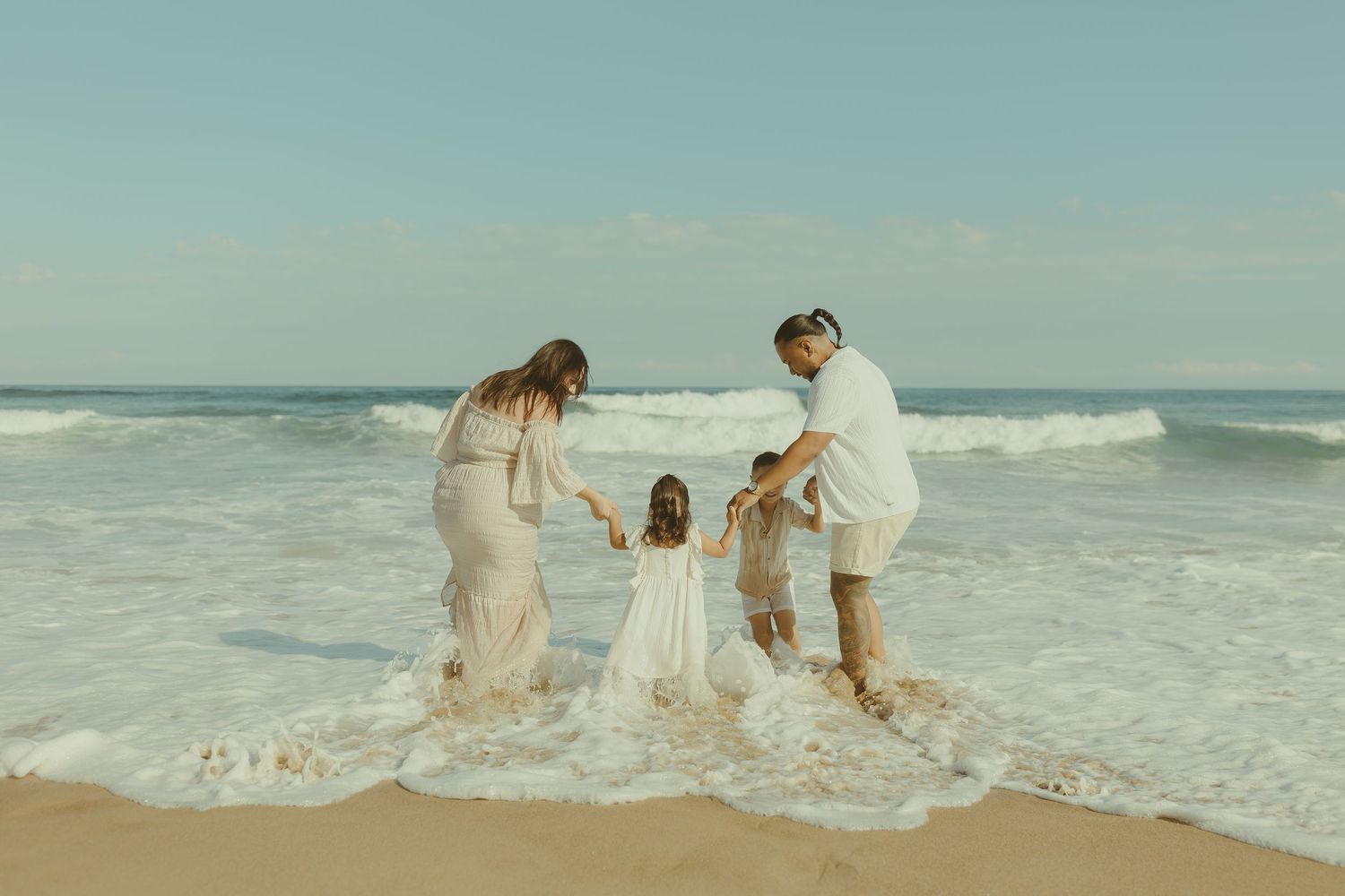 Group of people playing and splashing in ocean waves at sunset on a sandy beach.