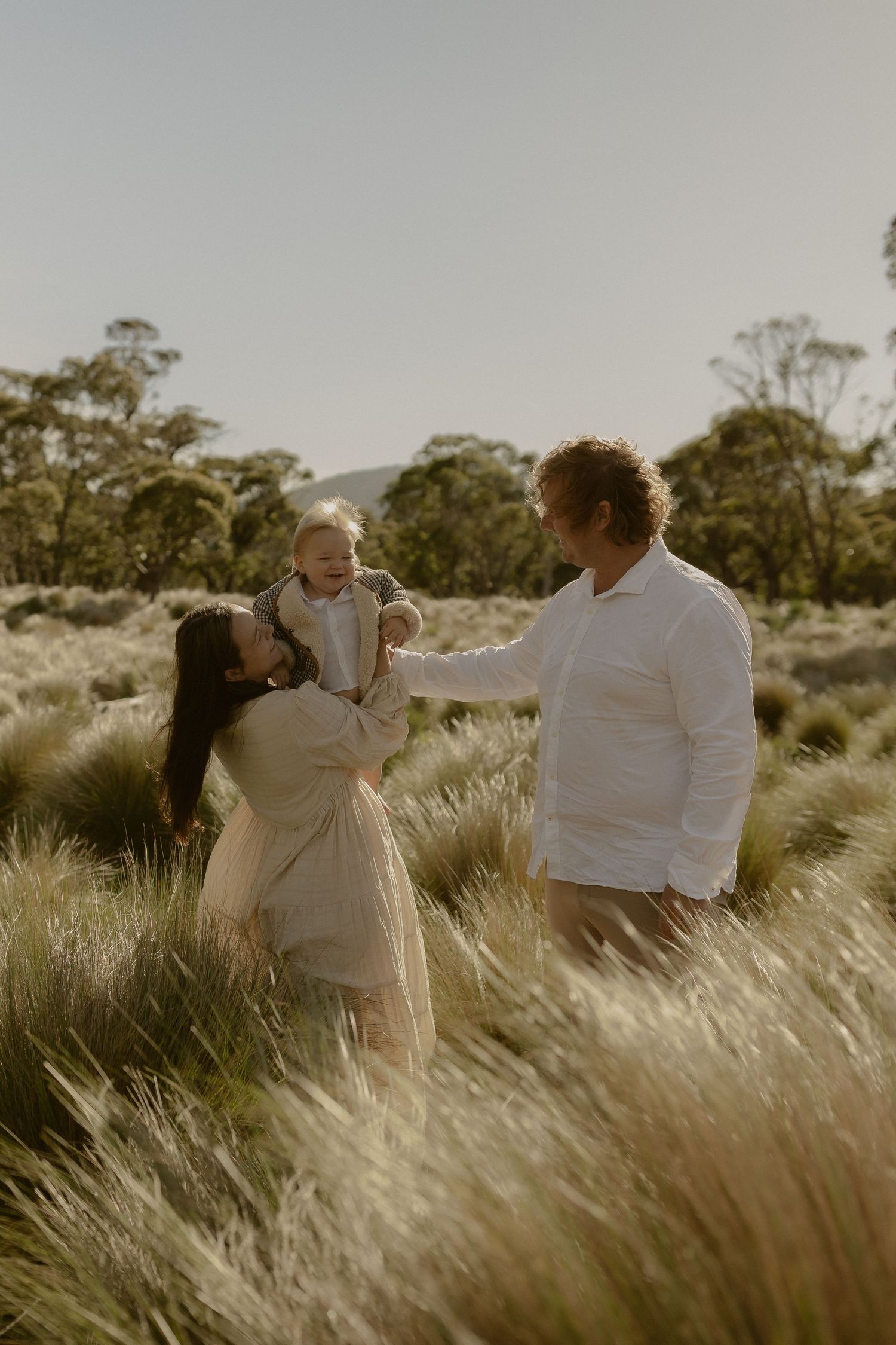A romantic couple embraces in a field of tall grass during golden hour sunset.