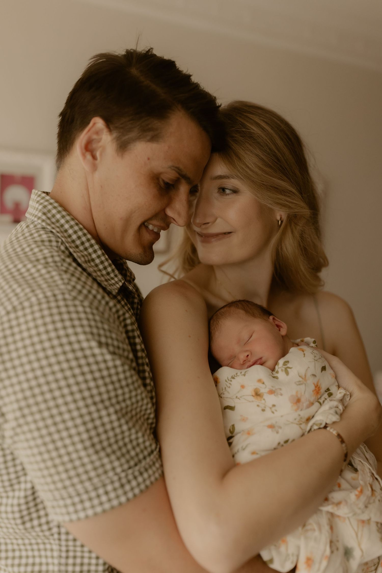 A couple shares intimate moments with their newborn baby in a warmly lit bedroom setting.