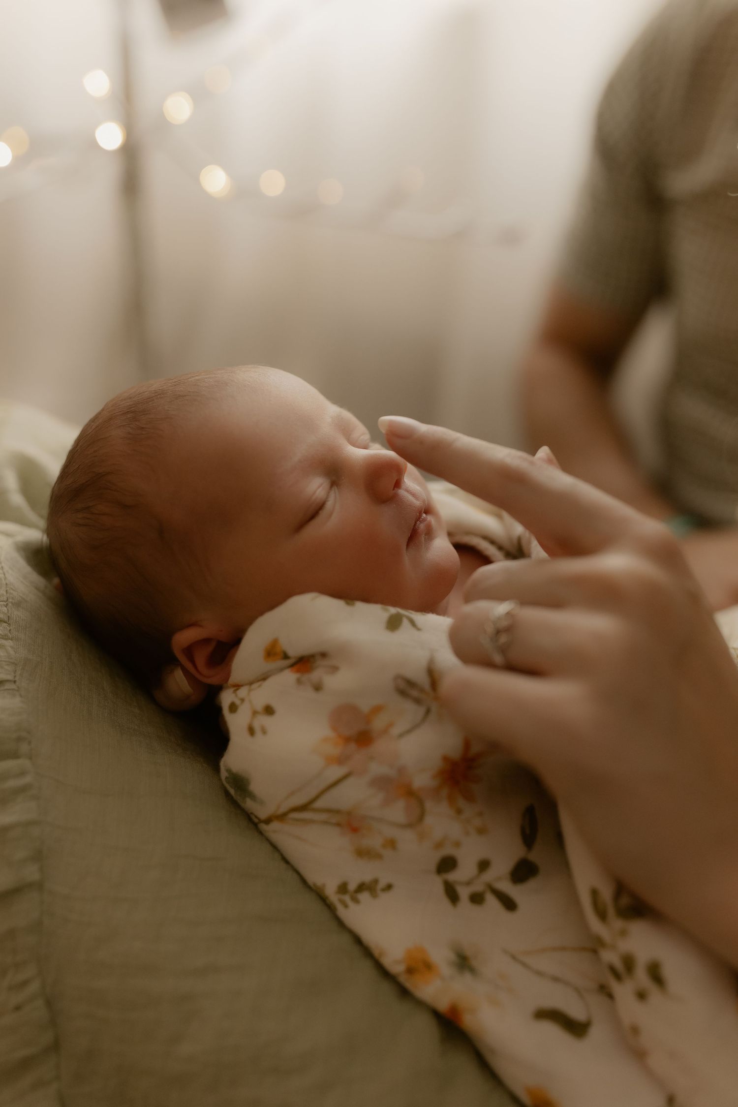 A newborn baby sleeps peacefully in a floral onesie while being gently cradled by caring hands.
