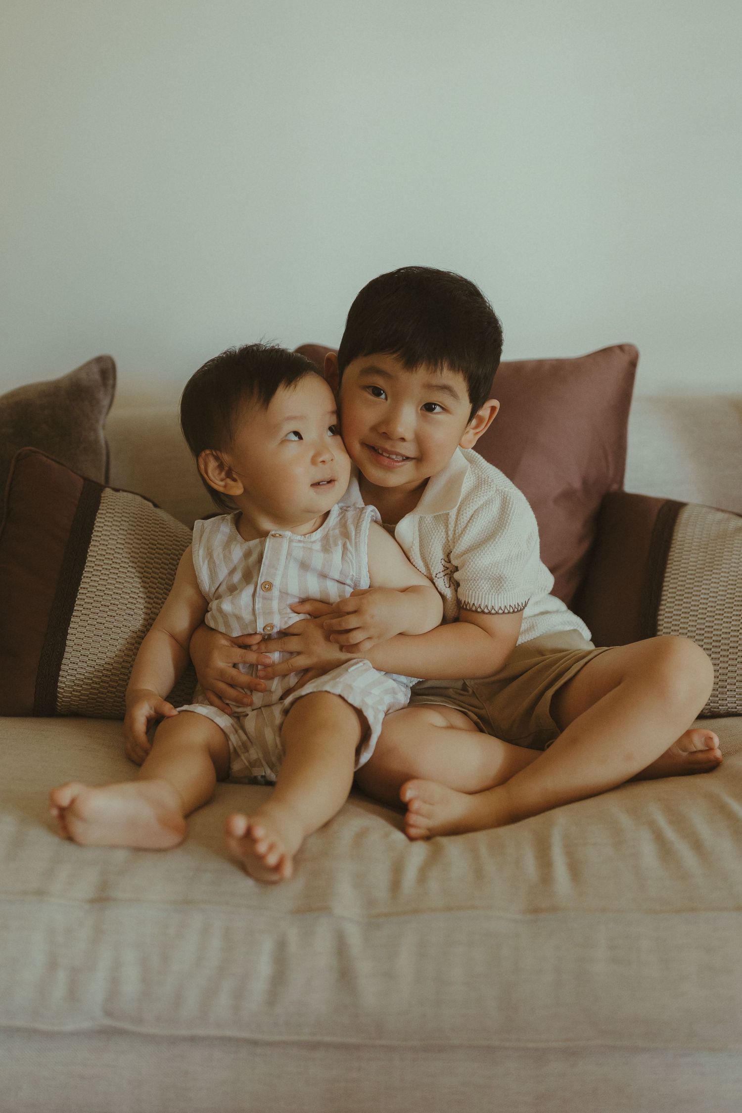 Two people sit together on a beige couch sharing a sweet moment in a series of candid photos.