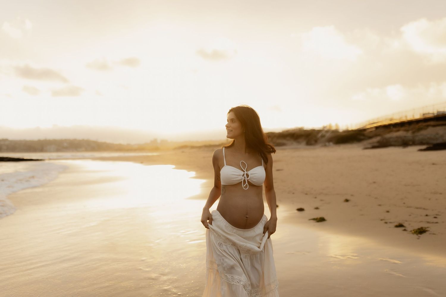 Golden sunset illuminates sandy beach with silhouettes and ocean waves in the background.