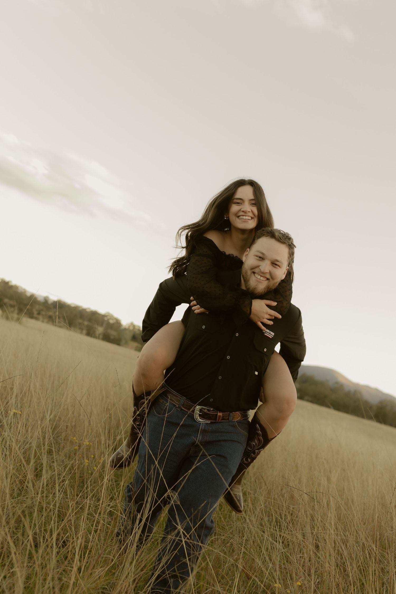 Man giving woman a piggyback ride through a scenic golden grass field at dusk.