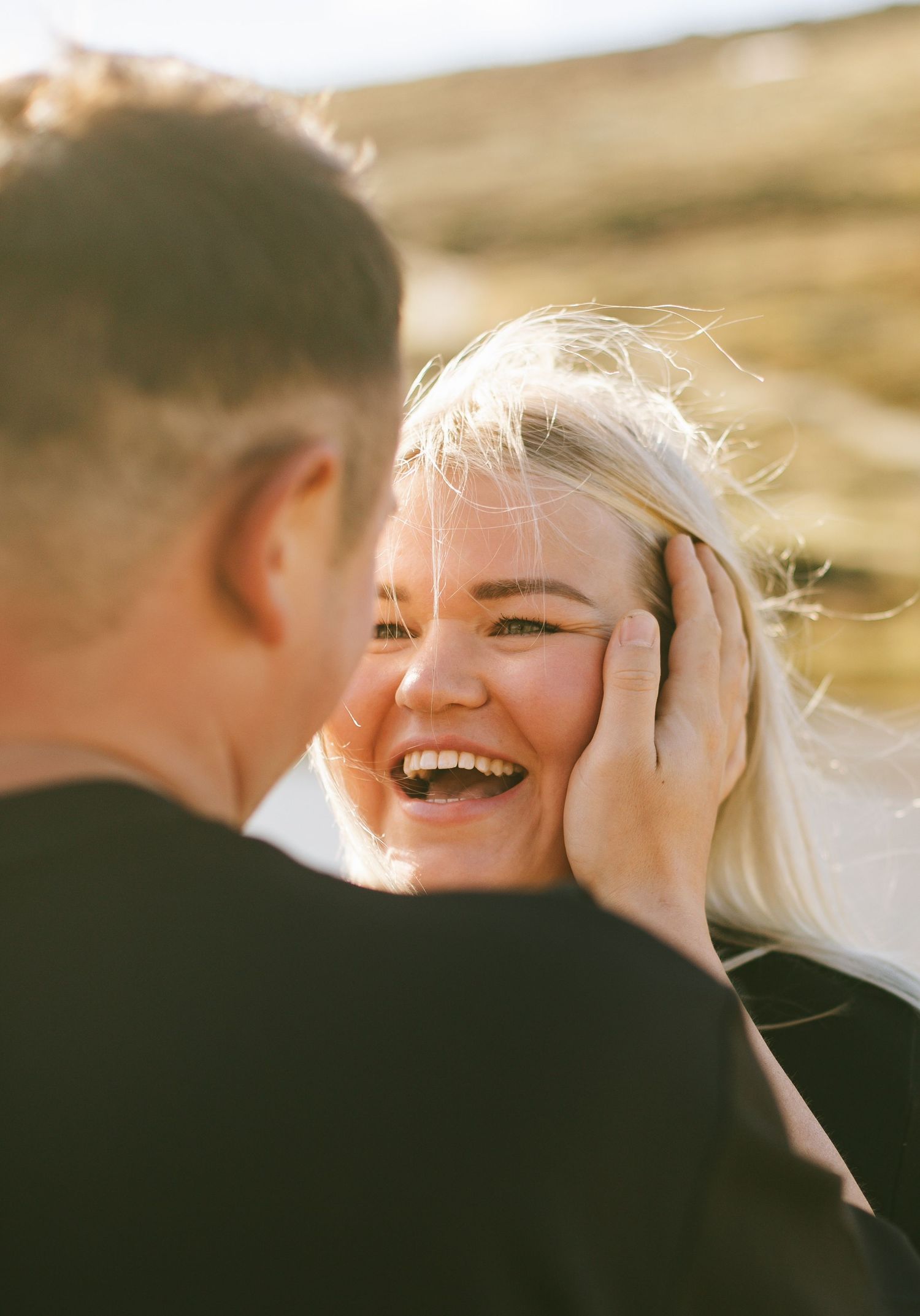 A romantic moment captured in golden sunlight shows a candid display of joy and laughter between a couple outdoors.