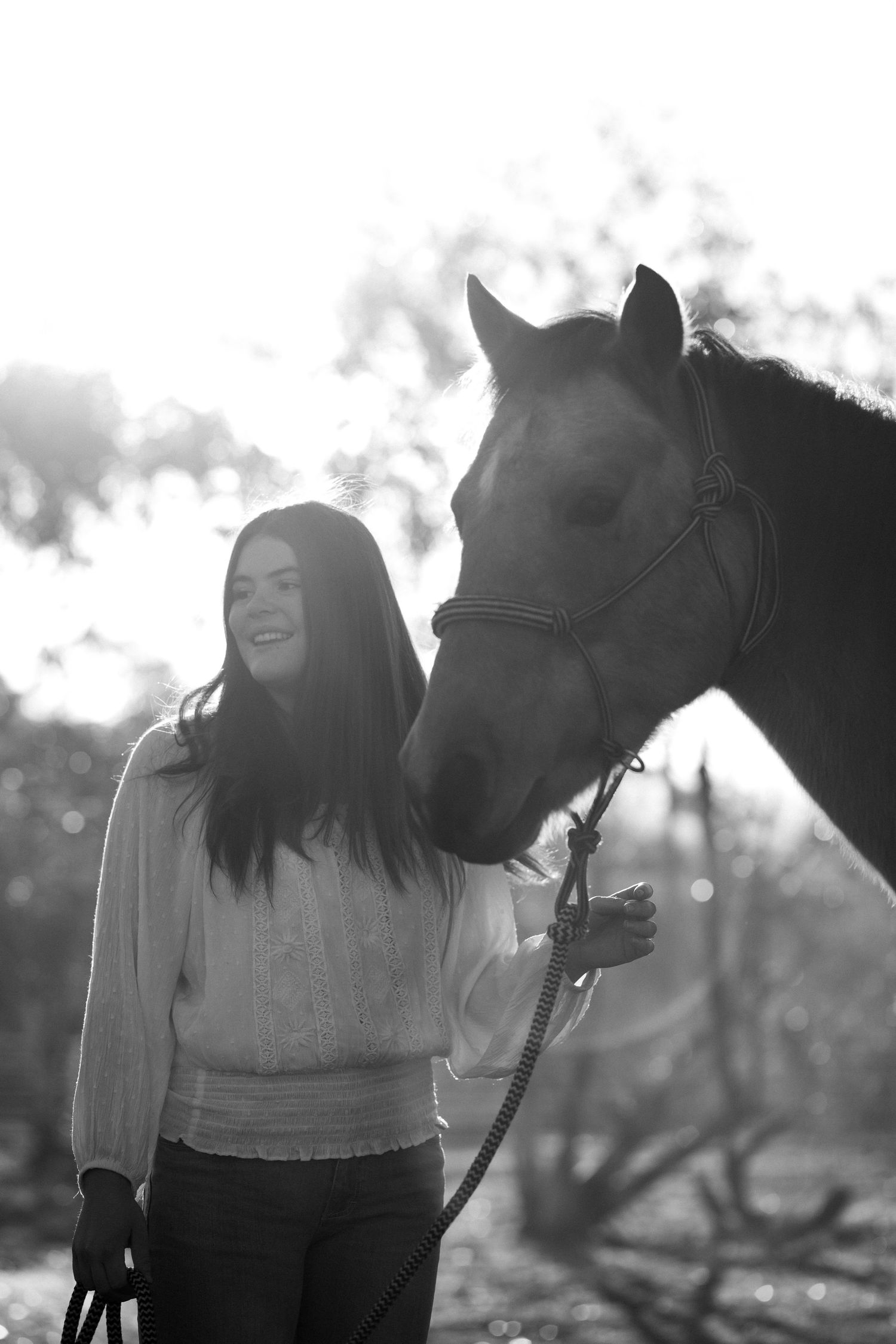 Black and white portrait of a joyful moment between a young woman and her horse against a cloudy sky.