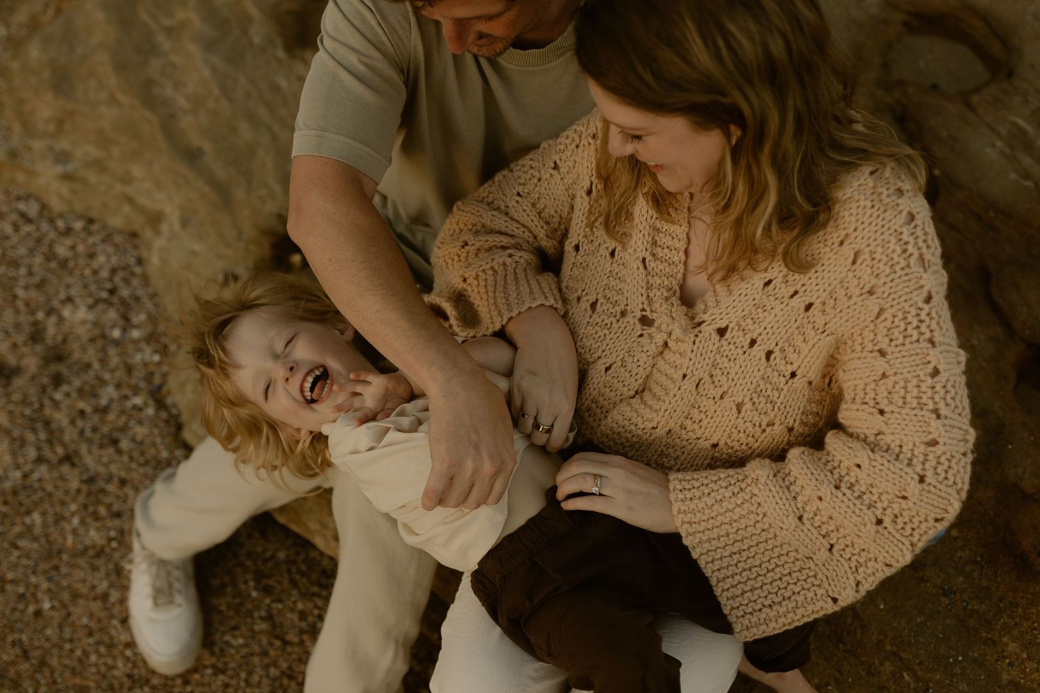 Parents laughing with their curly-haired toddler during a cozy family photo session outdoors.