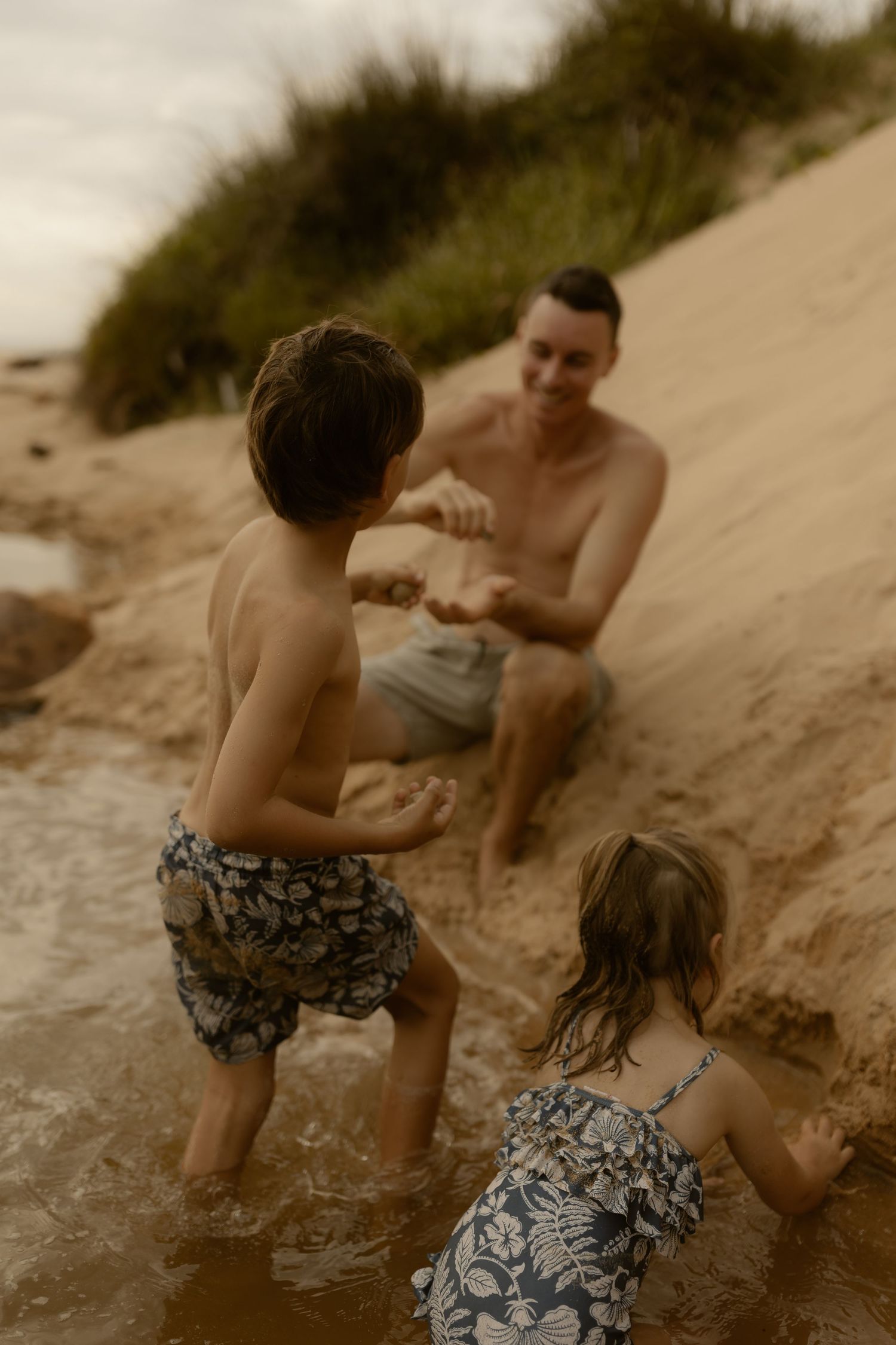 A family plays together at the water's edge of a sandy beach during sunset.