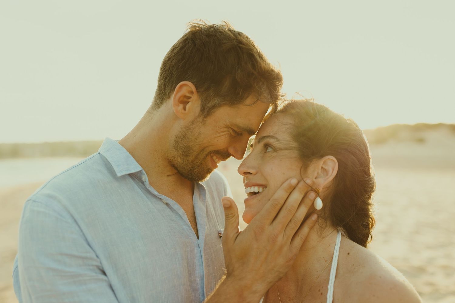 Intimate couple's portrait session at sunset on beach with soft golden lighting.