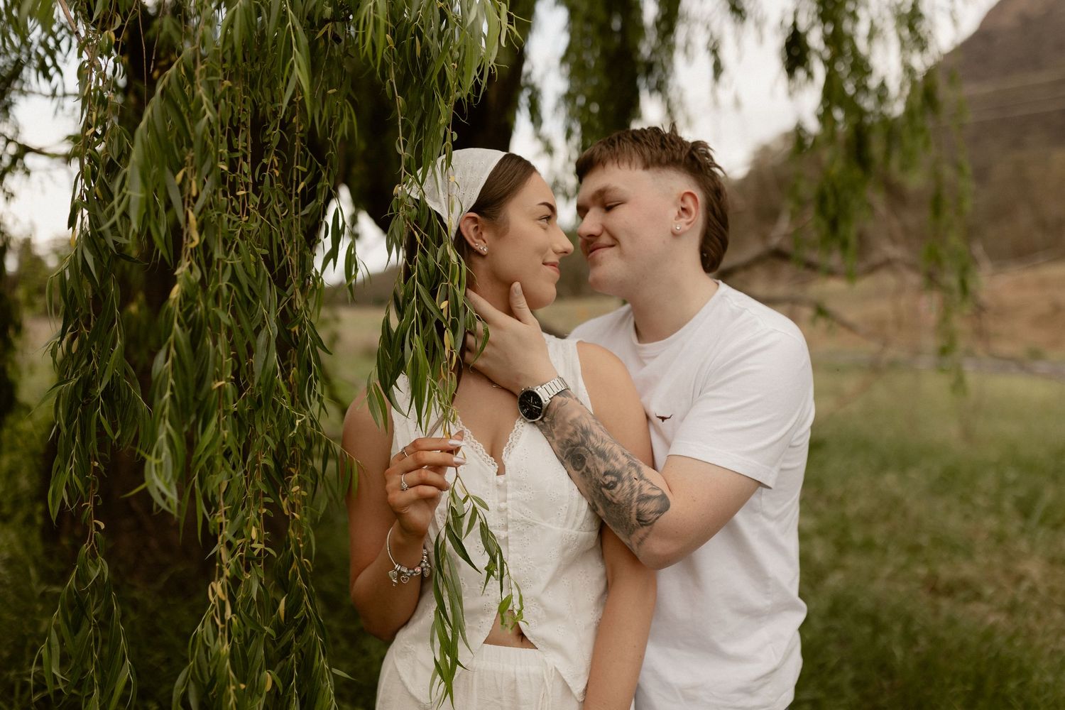 A romantic moment shared under the branches of a weeping willow tree.