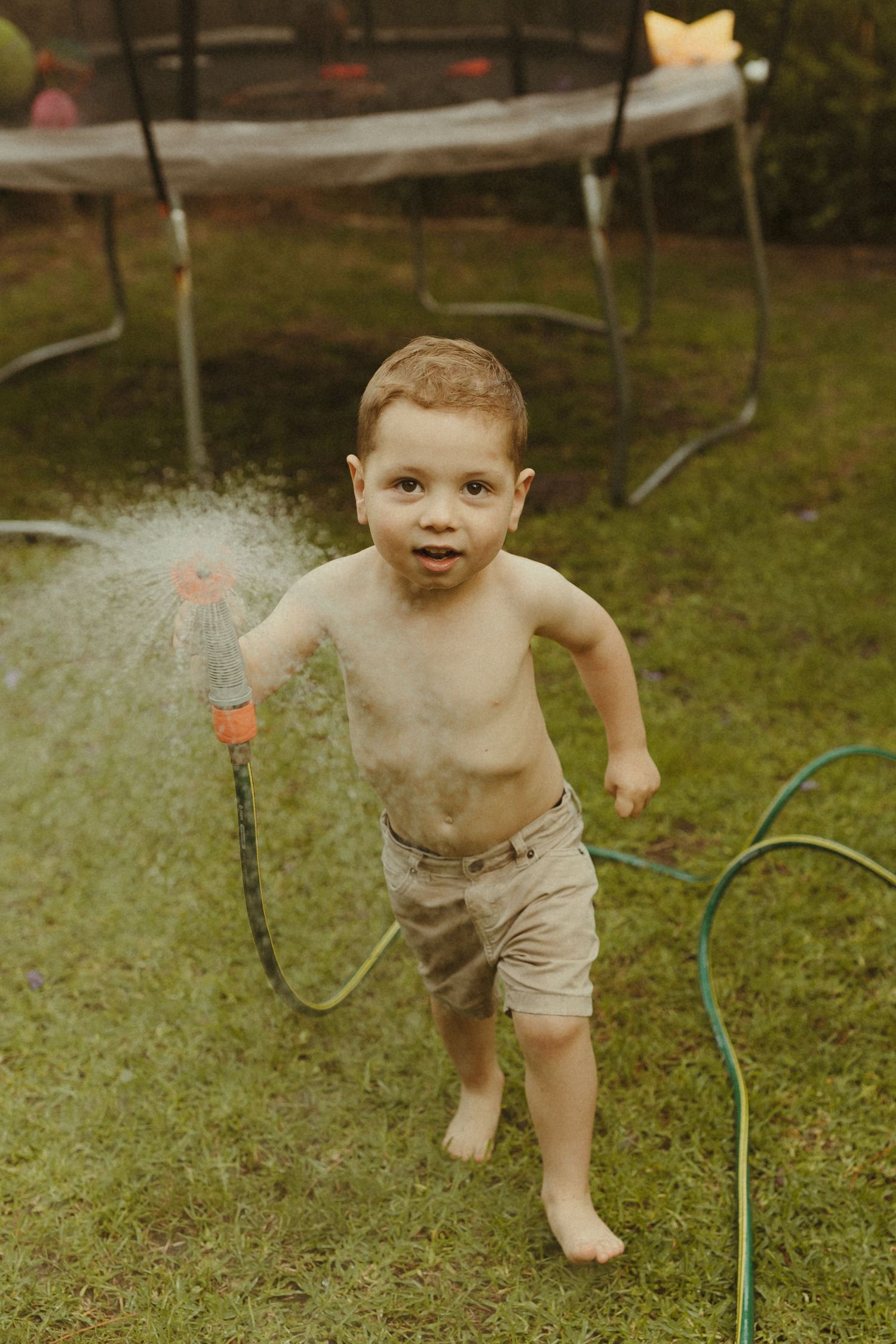 Young child running through water sprinklers in a backyard on a sunny day.