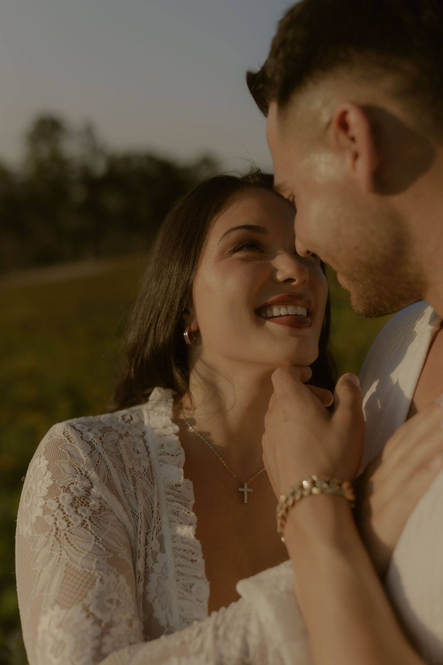 Romantic couple shares intimate moments in a field during sunset wearing elegant white attire.