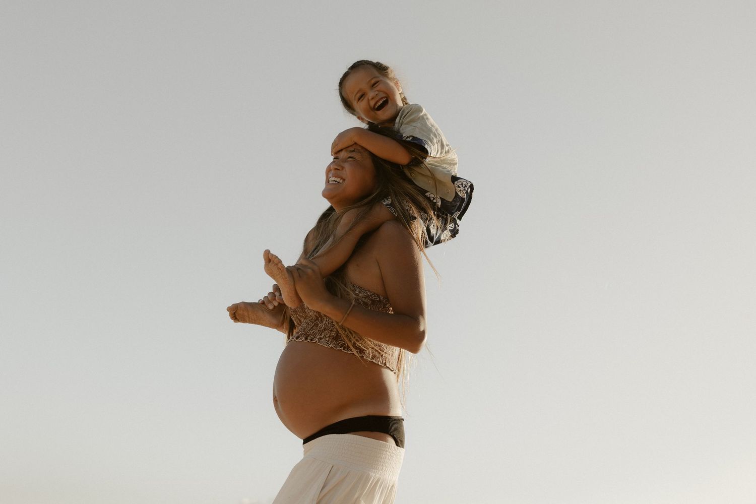Playful moment captured against bright sky with person being carried on shoulders.