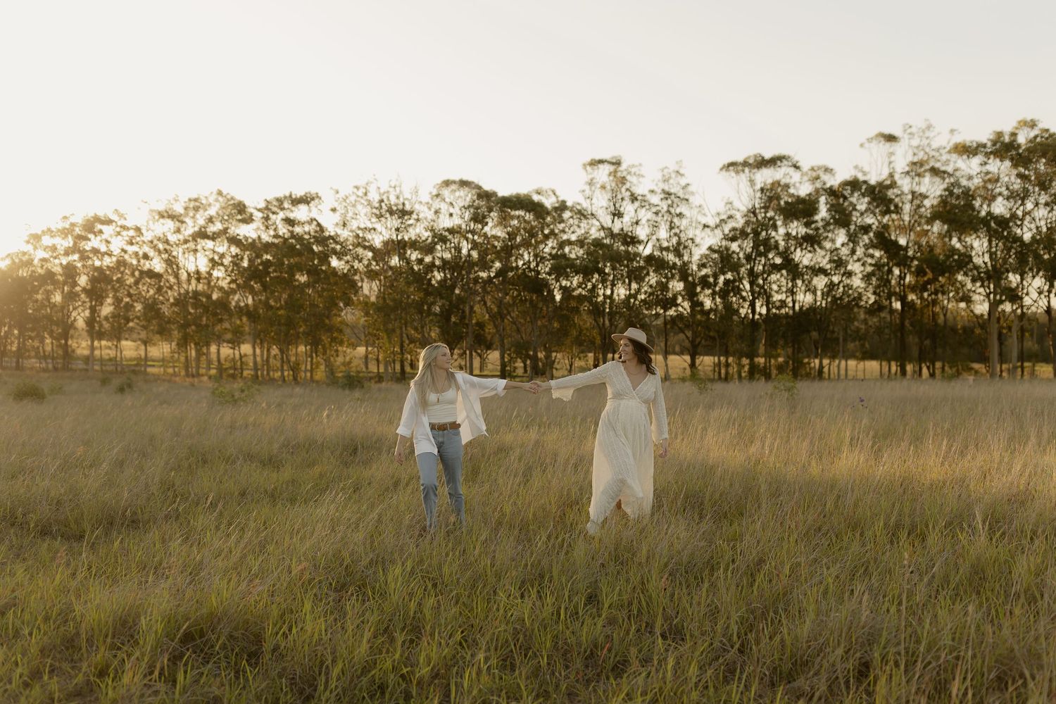 Silhouettes walking through tall grass in a rustic field at sunset with eucalyptus trees in background.