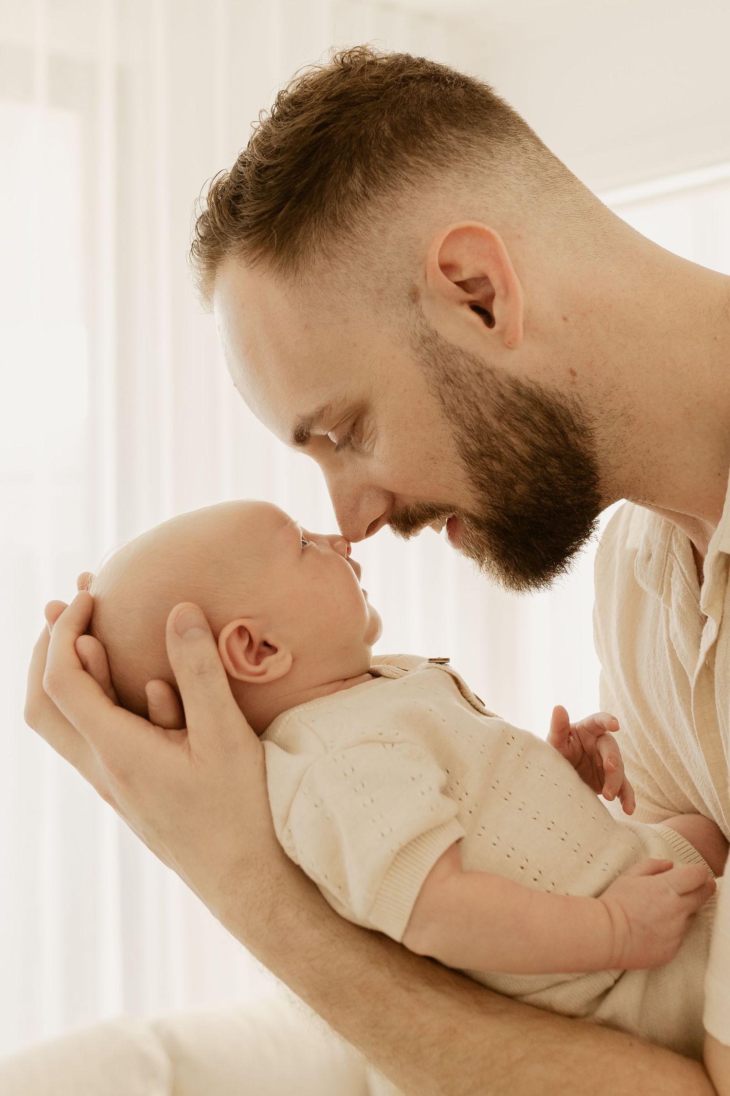 Tender moment between parent and infant as they share nose-to-nose contact in soft natural lighting.