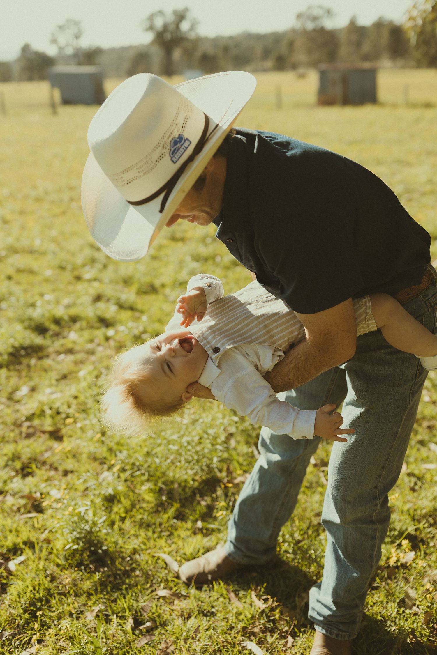 A playful moment captured in golden sunlight as a person in western wear dips a small child backward.