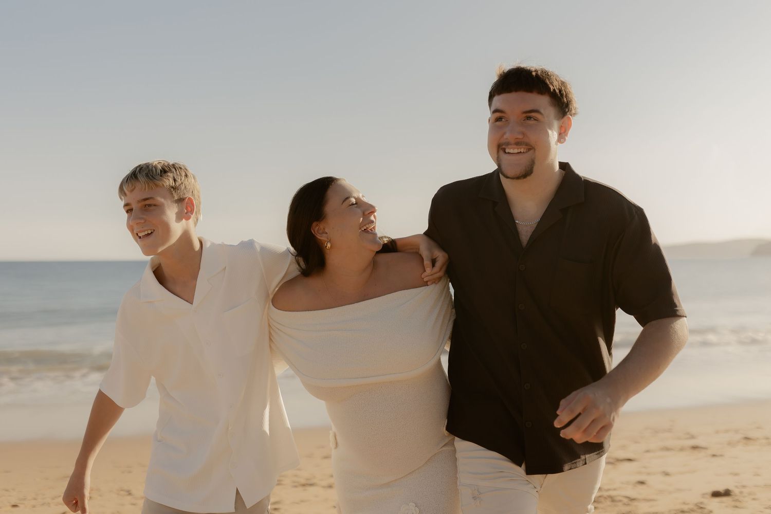 Romantic couple embraces on sandy beach during golden hour sunset photoshoot.