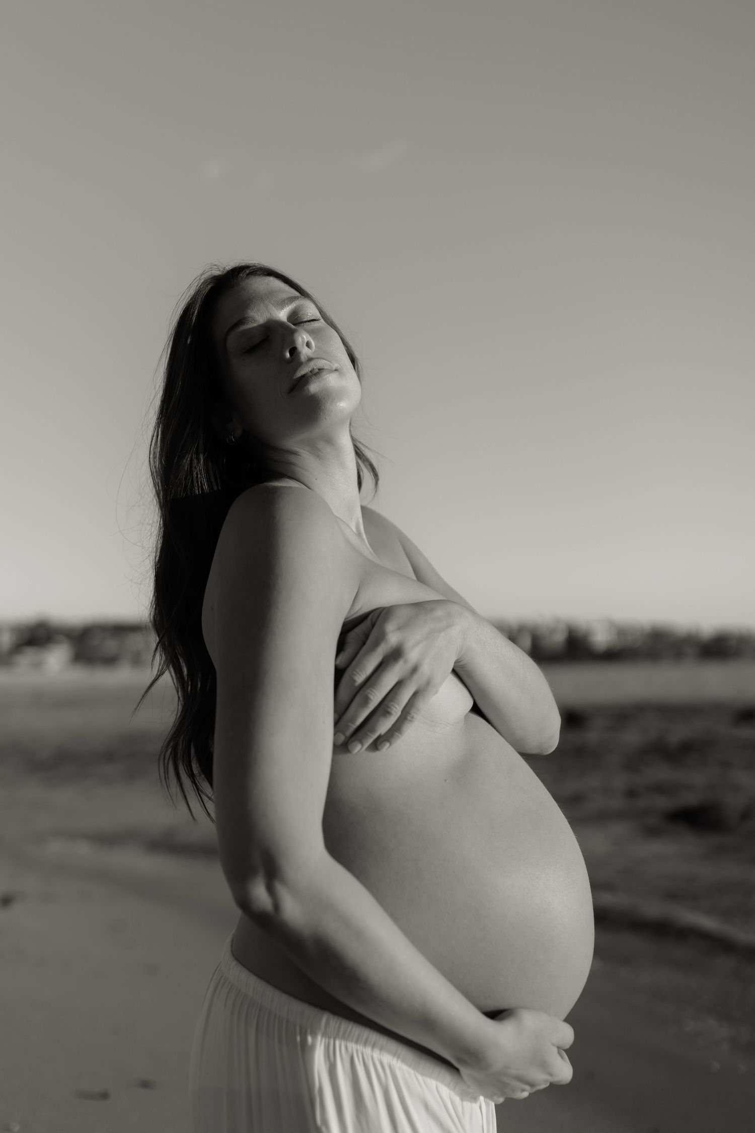 Artistic black and white maternity photos capturing intimate moments of pregnancy against a simple background.