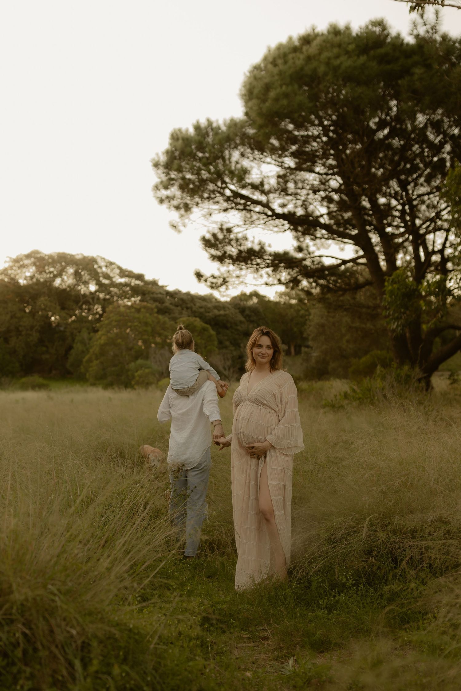 Couple walking together through a serene meadow at sunset in casual attire.