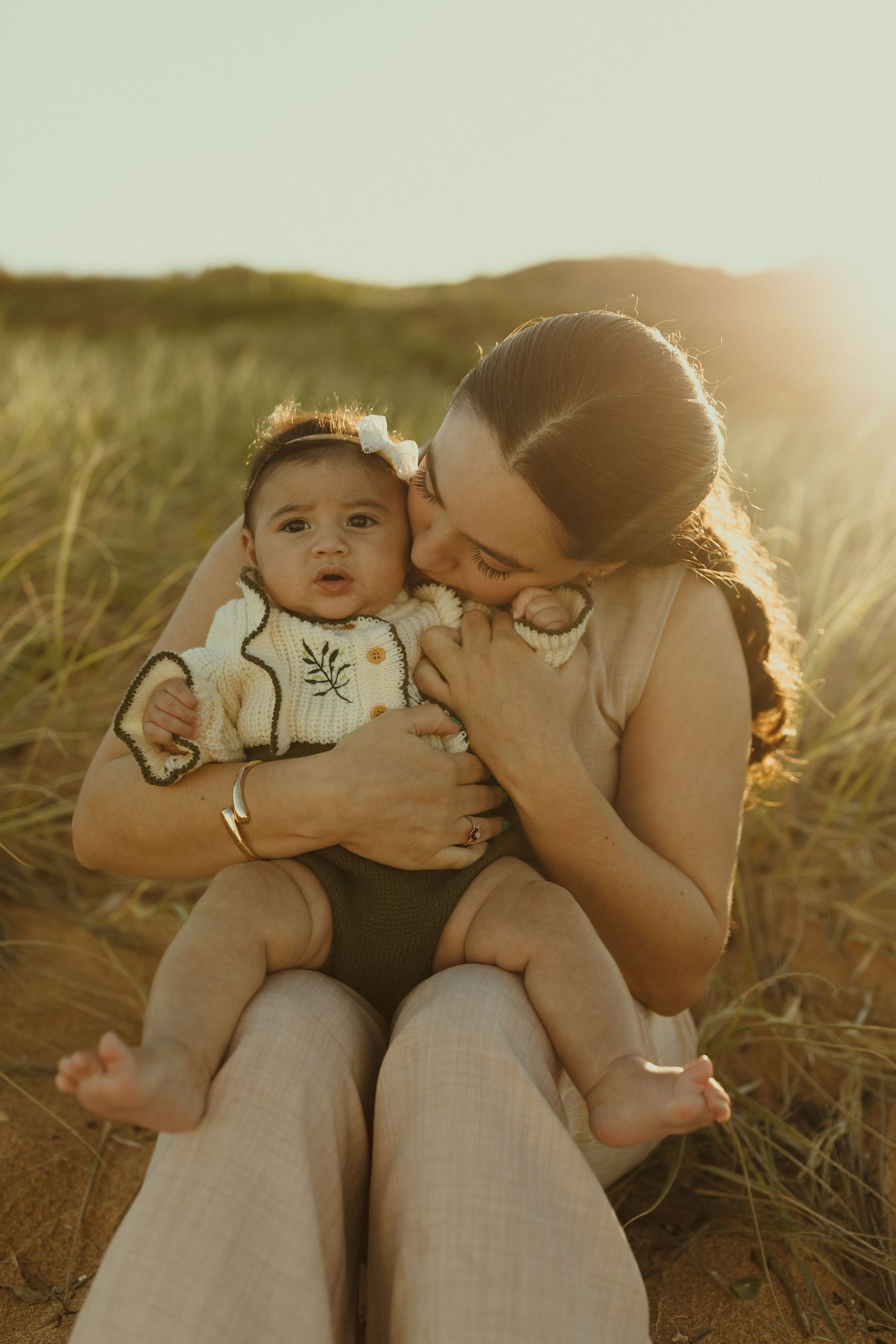 Parent and baby sharing tender moments together in golden sunlit field during outdoor photoshoot.
