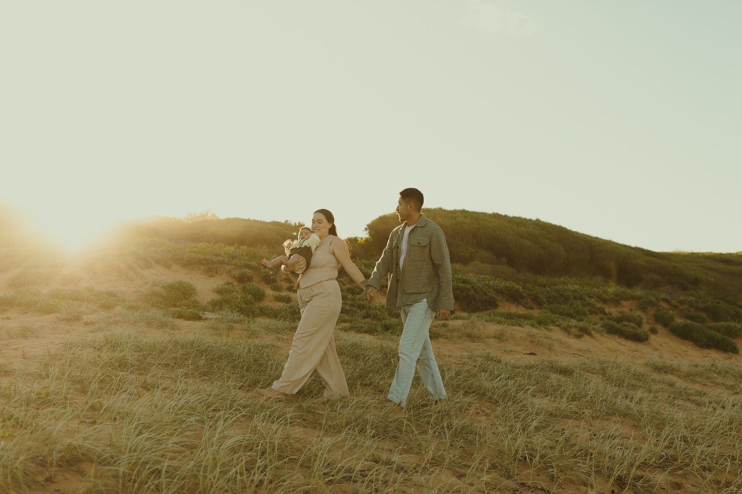 Two people walking together through rolling hills as golden sunlight bathes the grassy meadow at sunset.