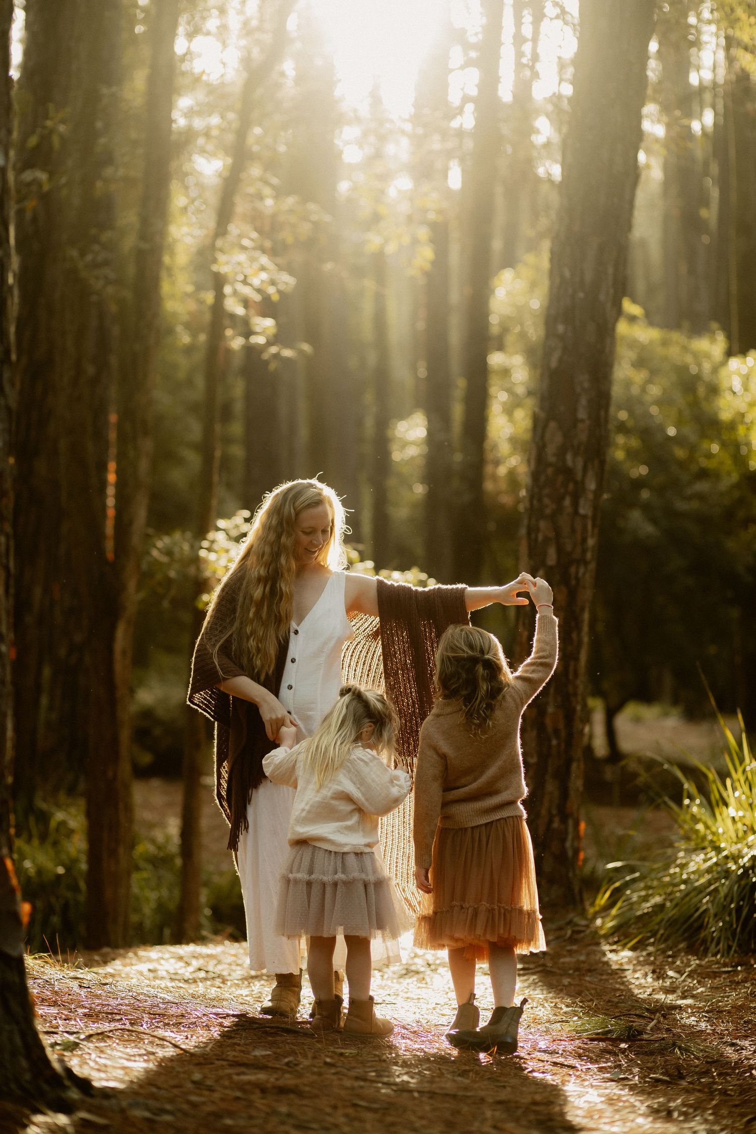 Three figures hold hands in golden forest light, creating a magical woodland moment.