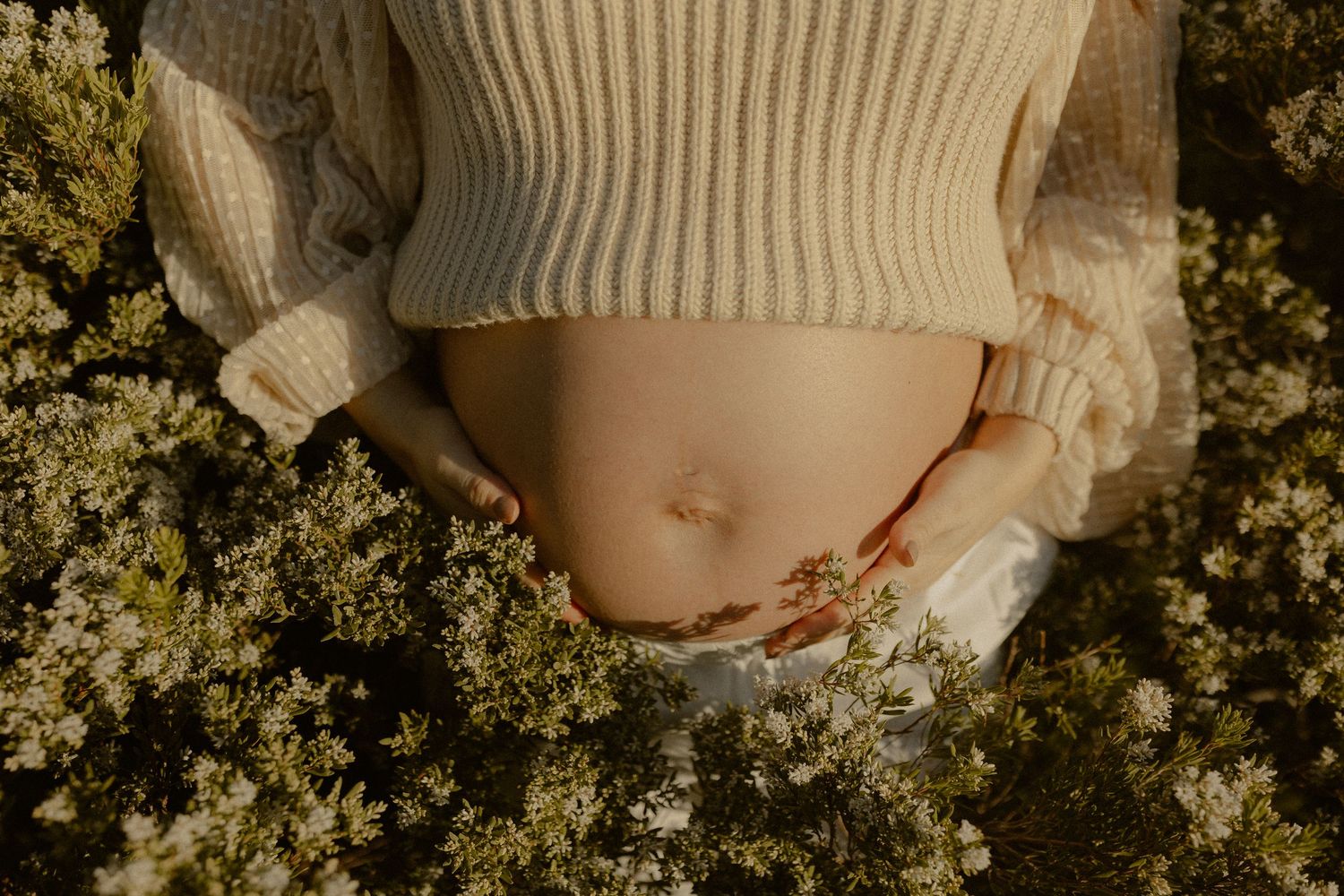 Delicate spring wildflowers frame a close-up artistic maternity portrait in soft natural lighting.