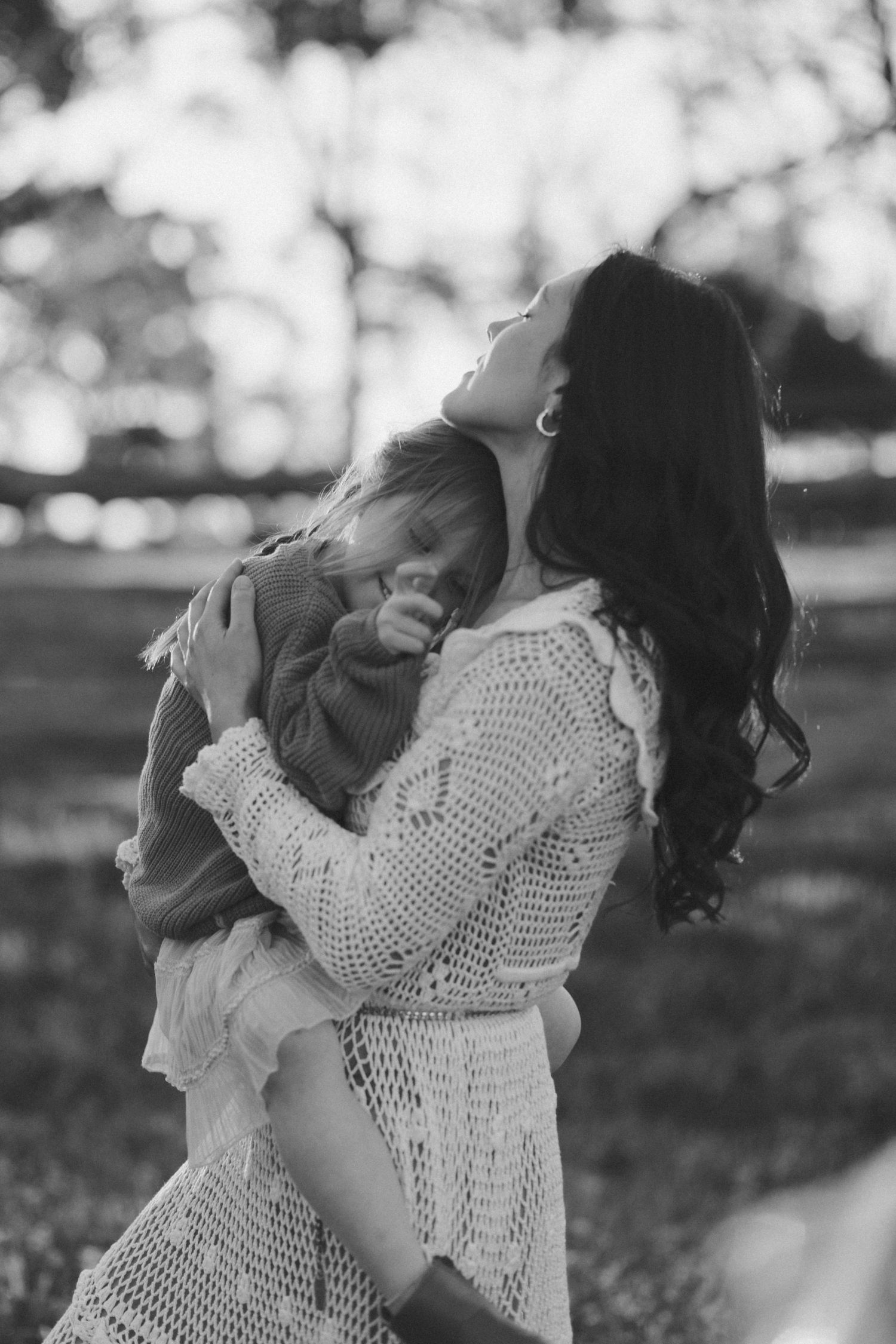 Black and white portrait of tender moment between parent and child in lace dress outdoors.