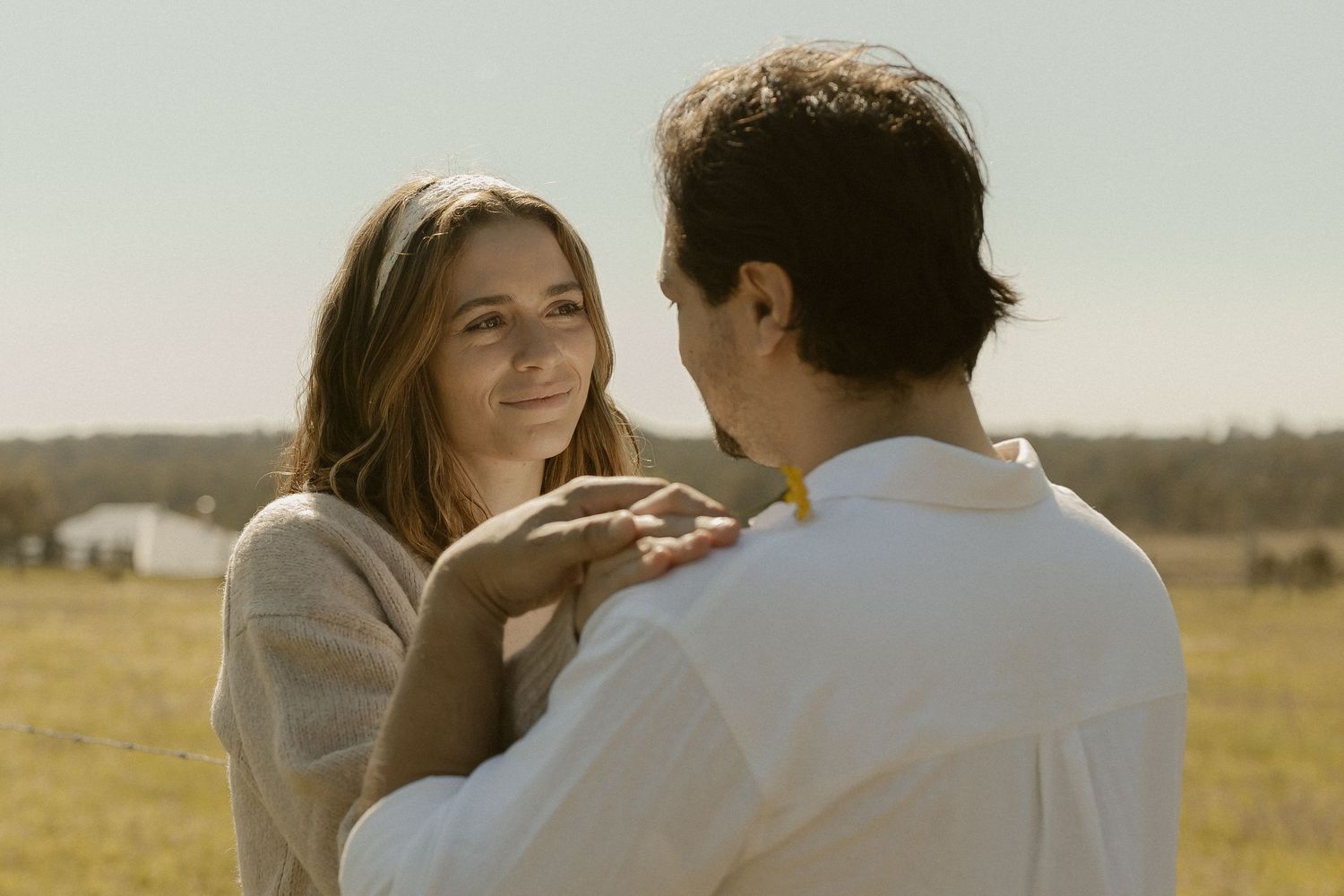 A couple shares an intimate romantic moment while standing in a sunny golden field at sunset.