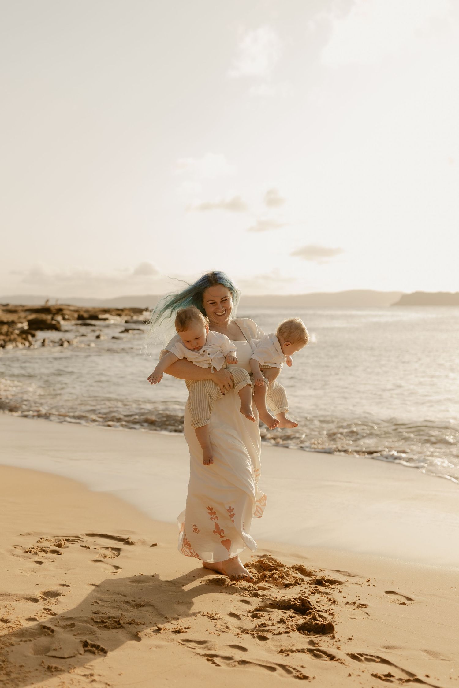 A couple in white clothing embraces lovingly on a sandy beach at sunset.