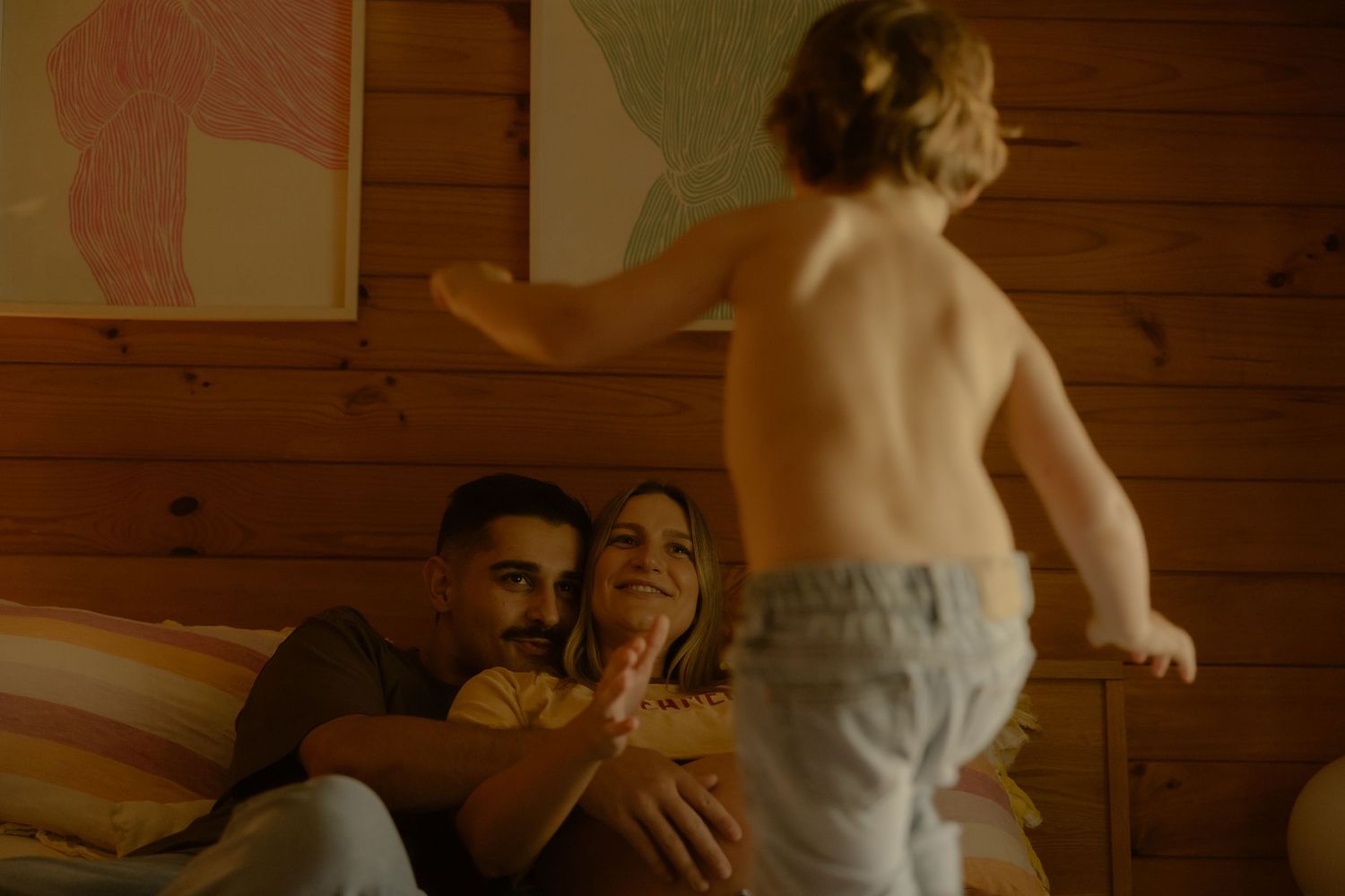 Happy couple relaxing on a bed while a toddler plays in front of them in a cozy cabin.