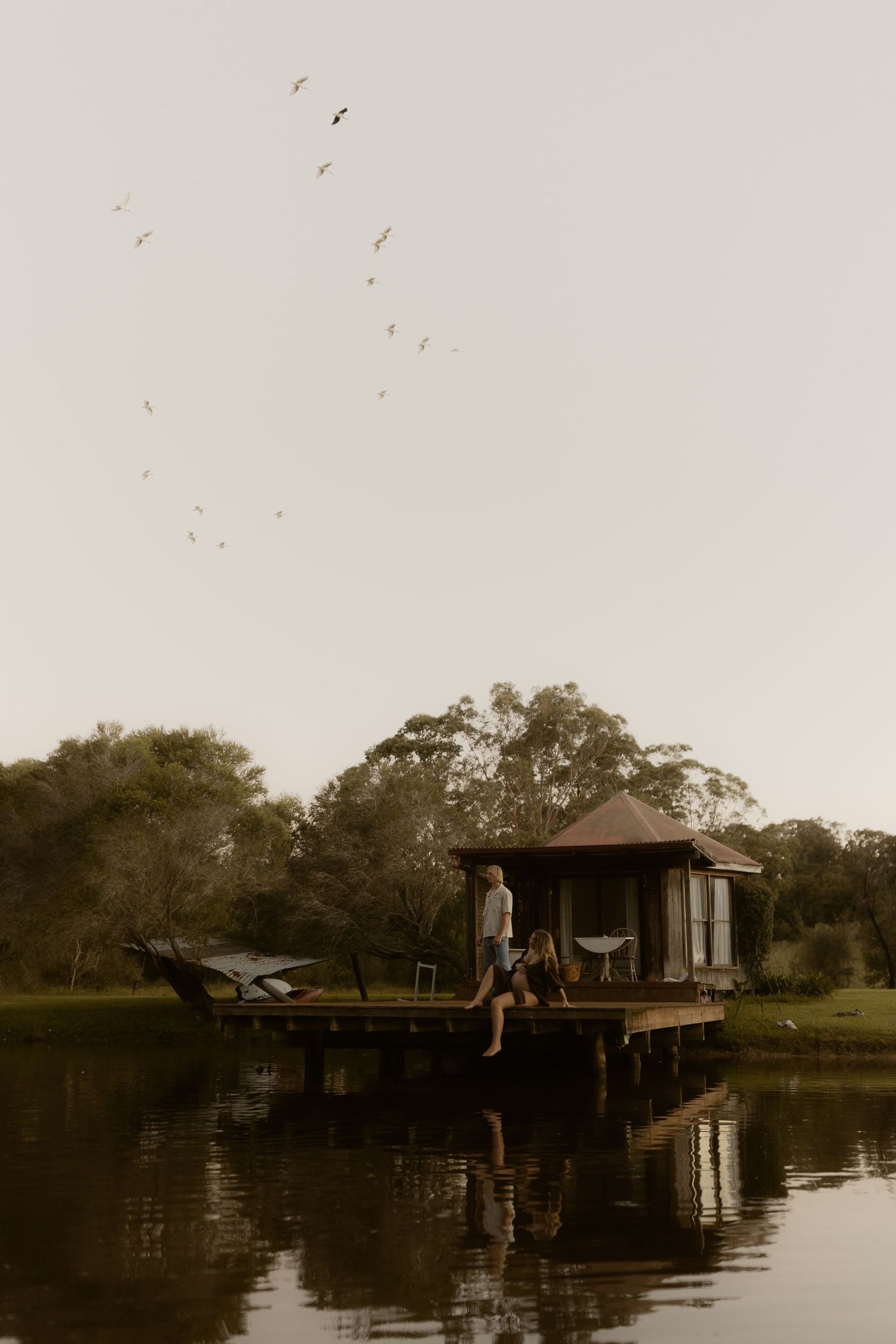 Rustic lake house on stilts reflected in calm waters at dusk.