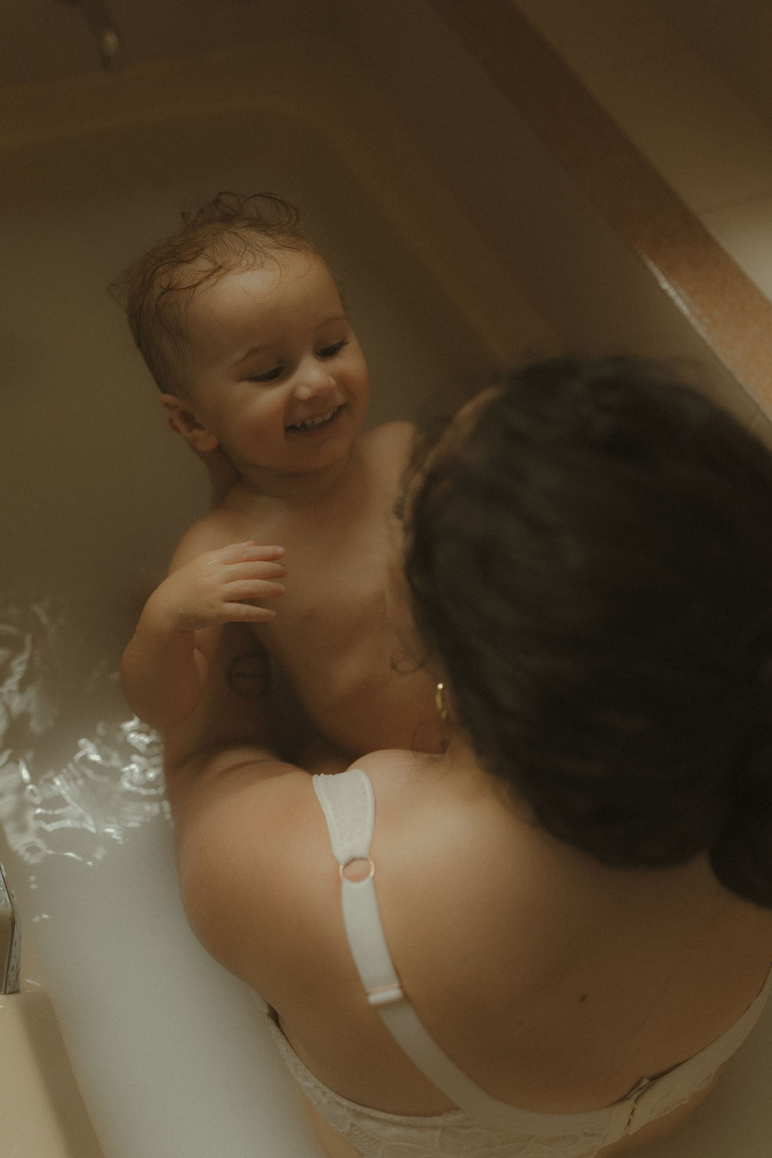Joyful bathtime moment captured between parent and laughing baby in warm tones.