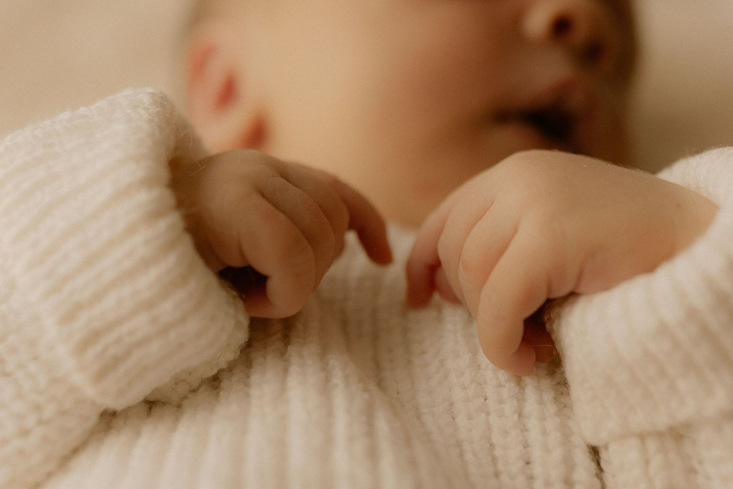 Small hands wearing a soft white knit sweater shown in warm tones against a light background.