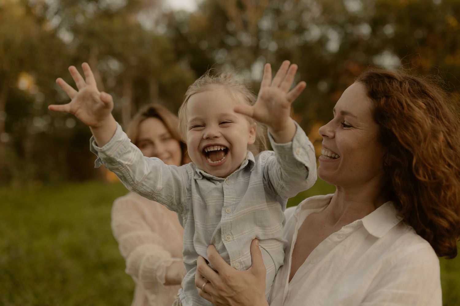 A joyful family shares laughter and embraces while playing together in a sunlit outdoor setting.