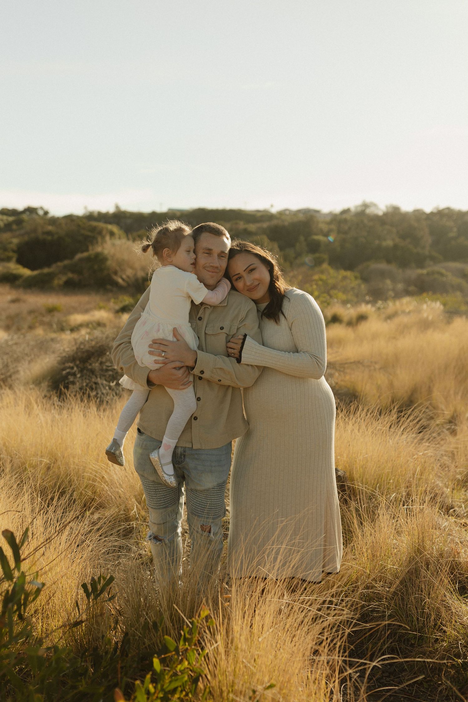 A family poses together in golden sunlit field with tall grass during sunset.