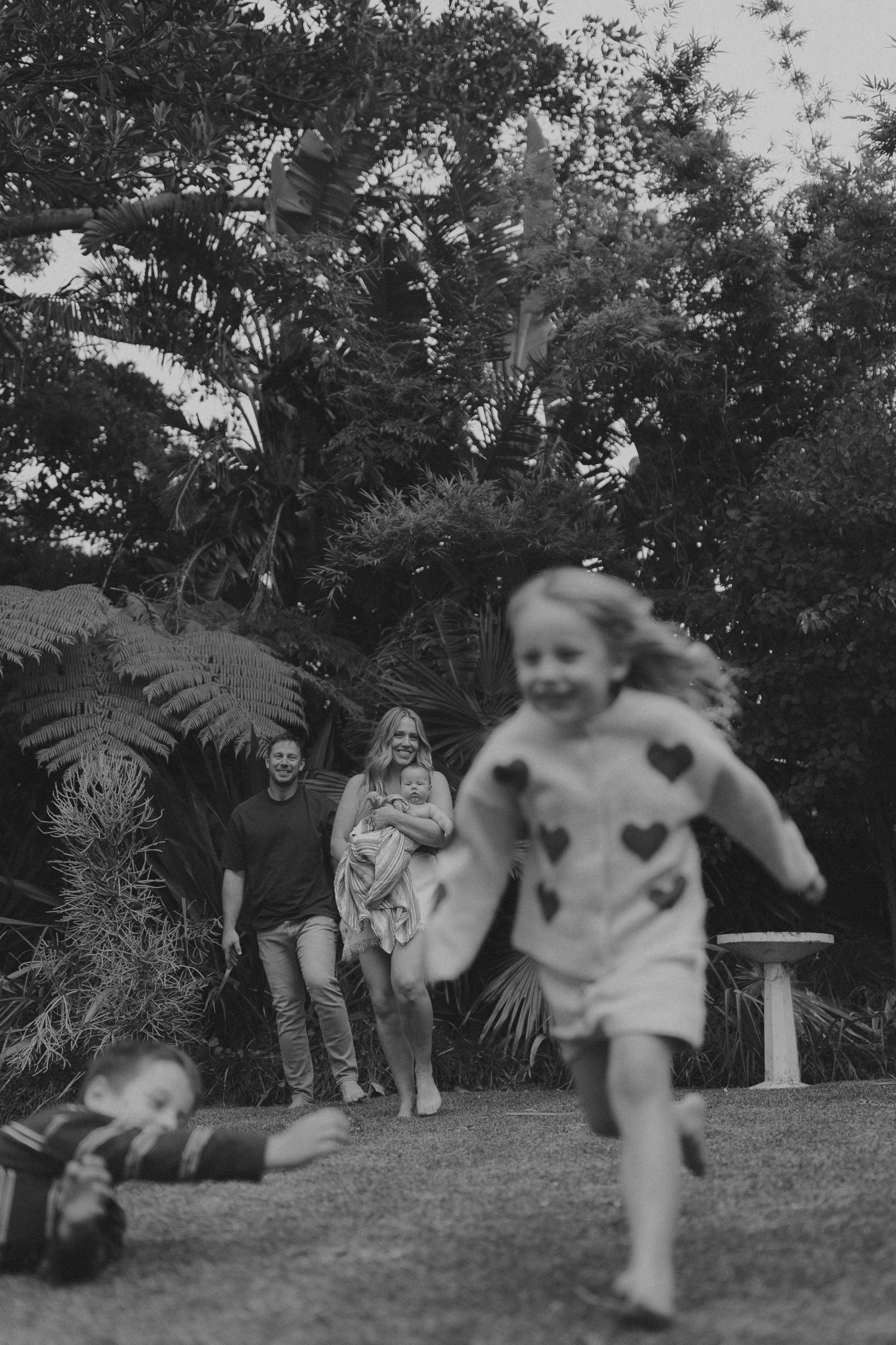 A young girl in a heart-print dress runs across a lawn while a family watches in black and white.